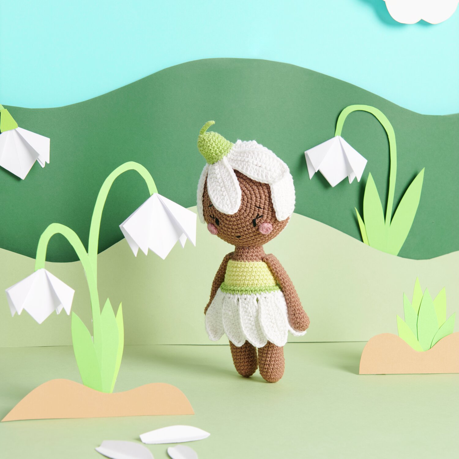 Creative Ricorumi dk: Gehäkelte Figur in einer Landschaft mit Blumen, in Nougat, Weiß und Pistazie.