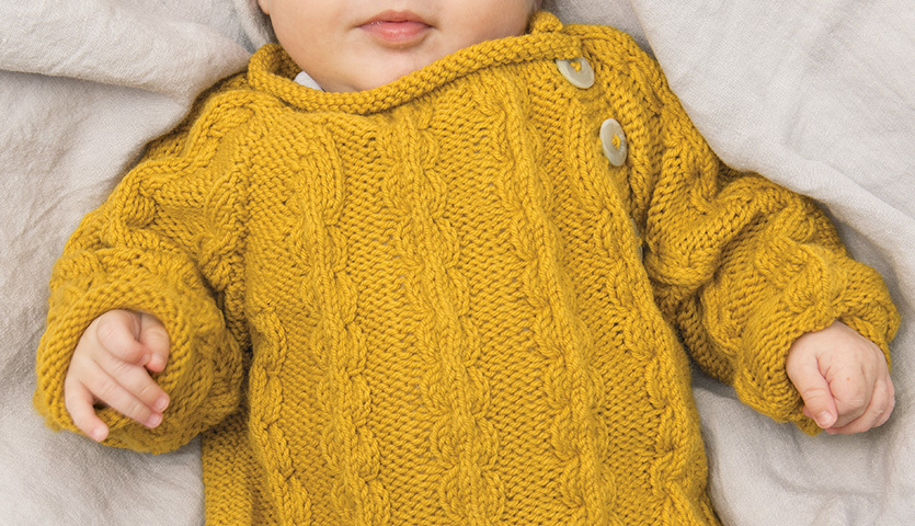 Strickanleitung Pullover aus Baby Classic DK: Baby in gelbem Strickpullover mit Zopfmuster und Knöpfen.