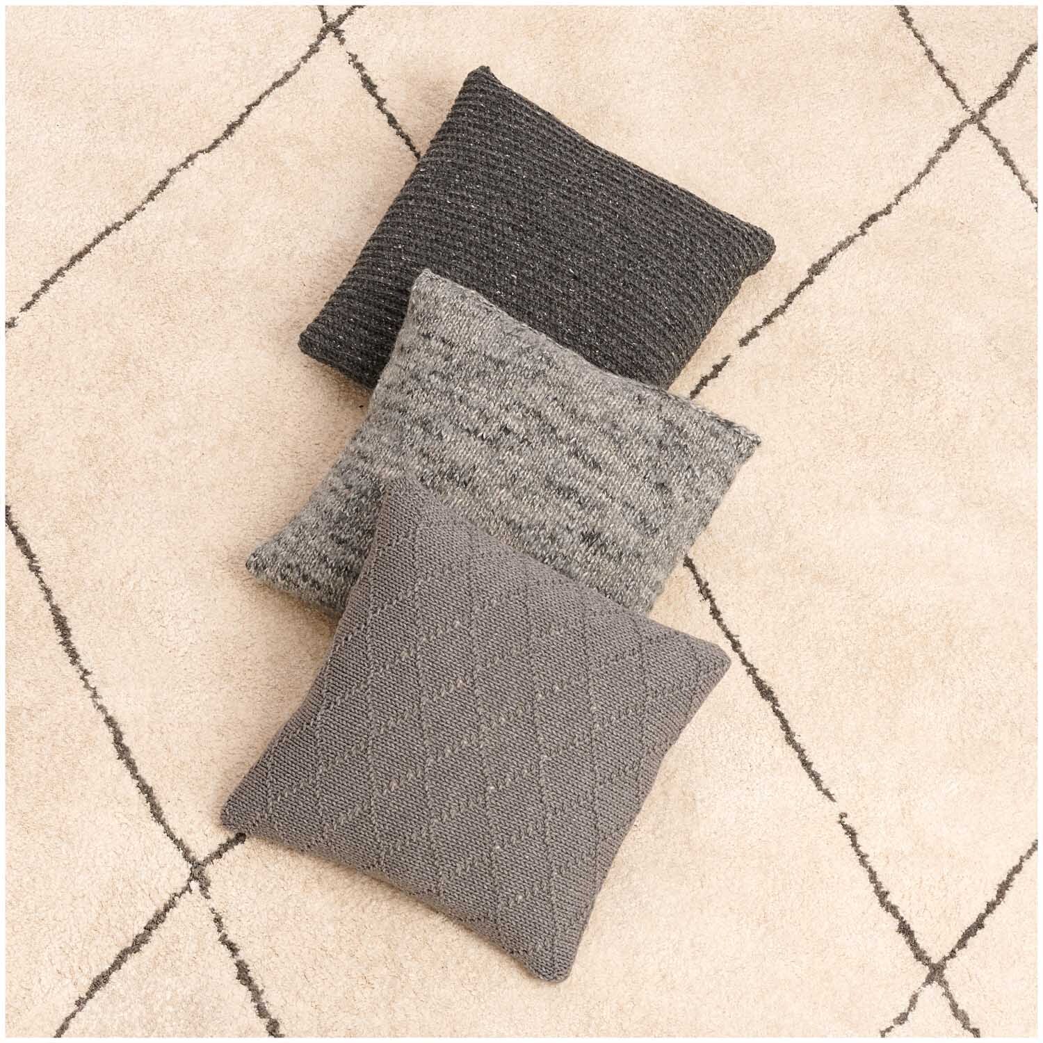 Fashion Modern Tweed aran: Drei stilvolle Kissen in verschiedenen Grautönen auf einem beigen Teppich. Ideal für modernes Wohndesign.