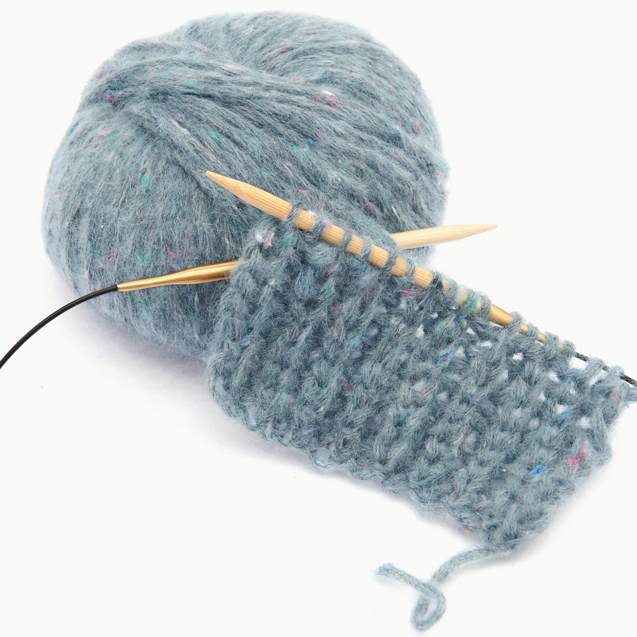 Ein Strickstück auf Rundstricknadeln mit dem zugehörigen blauen Wollknäuel. Flatlay von Produkten.
