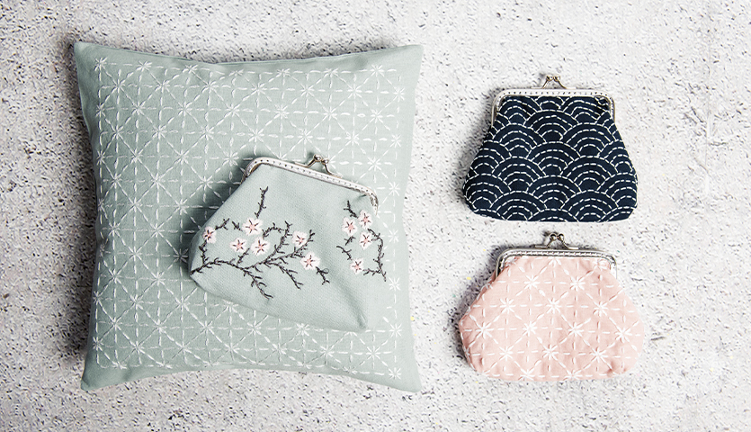 Nähanleitung Sashiko Etui: Drei bestickte Etuis in Pastellfarben auf einem Kissen mit geometrischem Muster.