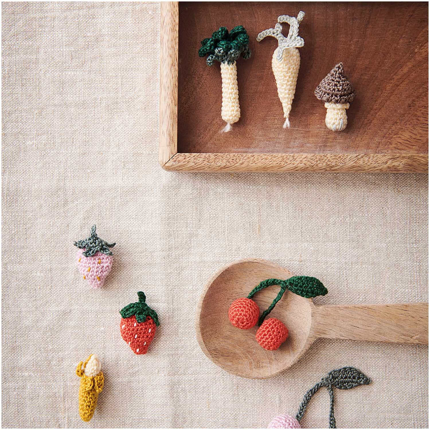 Essentials Crochet: Gehäkelte Früchte und Gemüse auf Leinen, präsentiert in Holzschale und Löffel.