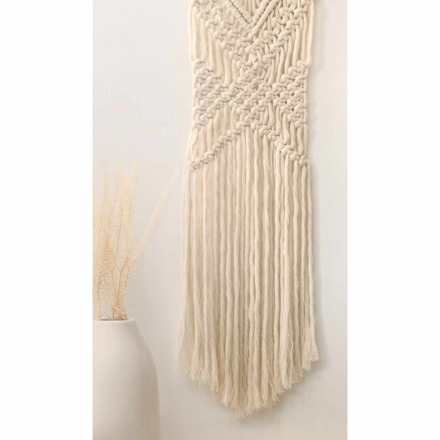 Makramee-Set Boho: Wandbehang aus cremefarbenem Garn, 10-teilig, neben einer Vase mit Trockenblumen.