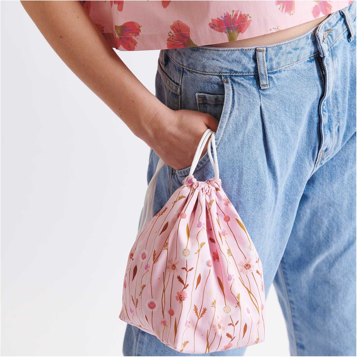 Meterware Druckstoff Wildblumen rosa: Frau in Jeans hält rosa Beutel mit Wildblumenmuster von Rico Design.