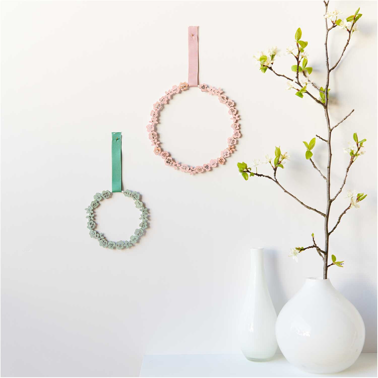 Holzstreu Blüte 48 Stück: Zwei dekorative Kränze in Pastelltönen an einer weißen Wand.