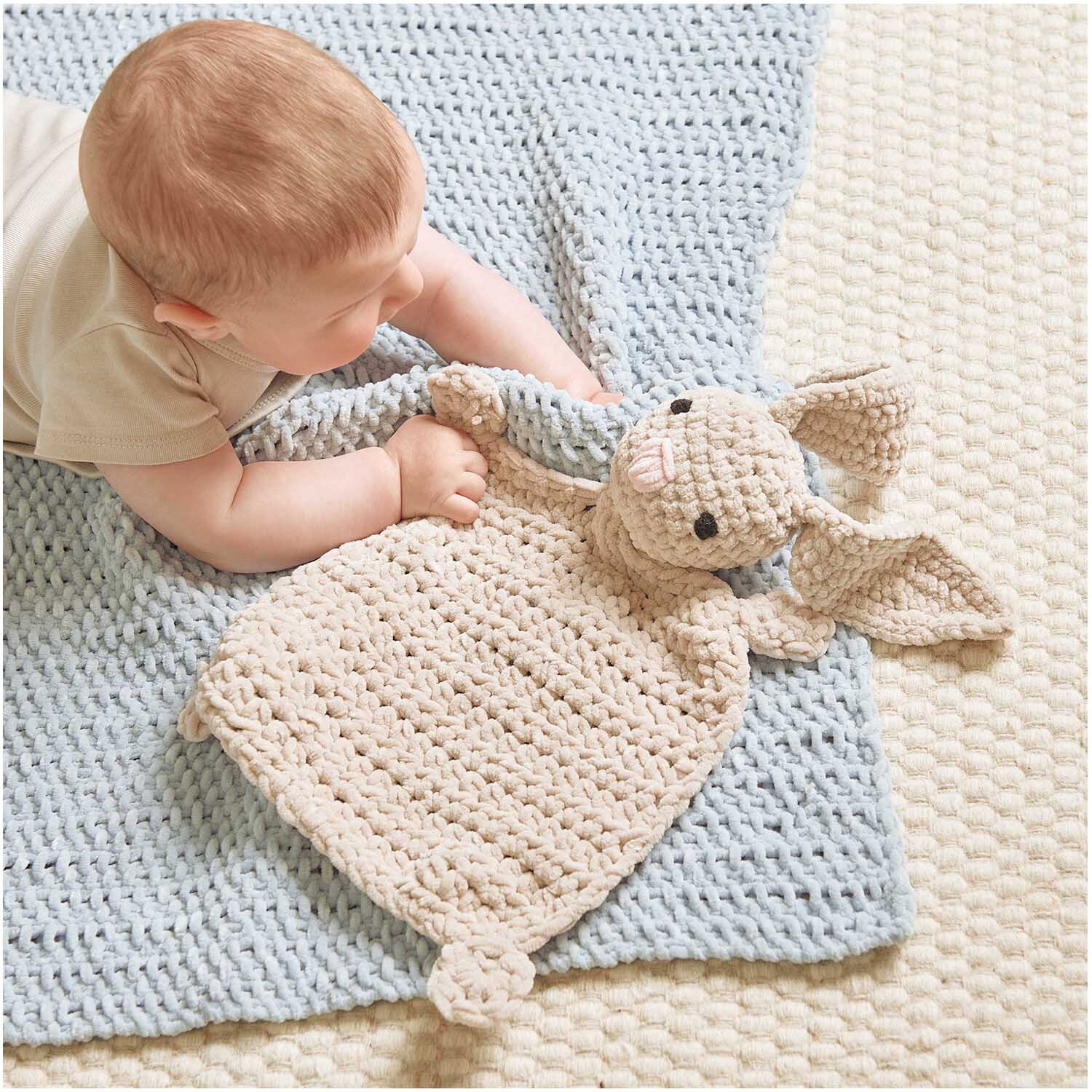 Creative Chenillove: Ein Baby spielt auf einer hellblauen Decke mit einem gestrickten Kuscheltier. Ideal für Kinderzimmer.