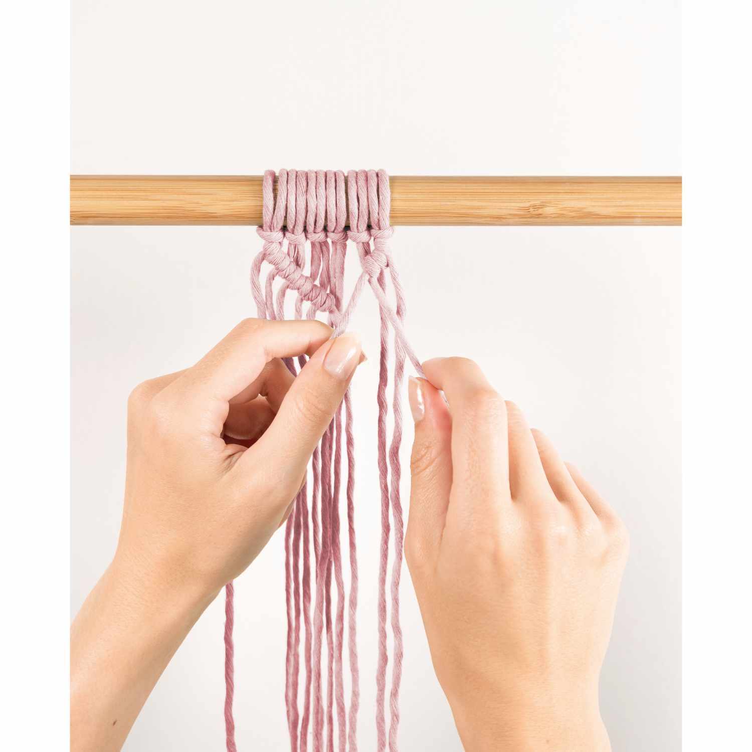 Makramee-Set Boho: Hände knüpfen rosa Fäden an einem Holzstab, 10-teiliges Set von folia.