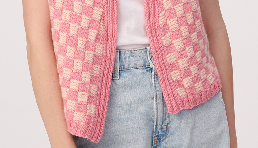 Strickanleitung Damenweste aus Creative Cotton Fleece dk: Rosa-weiße karierte Weste, kombiniert mit blauer Jeans, ideal für Freizeitlooks.