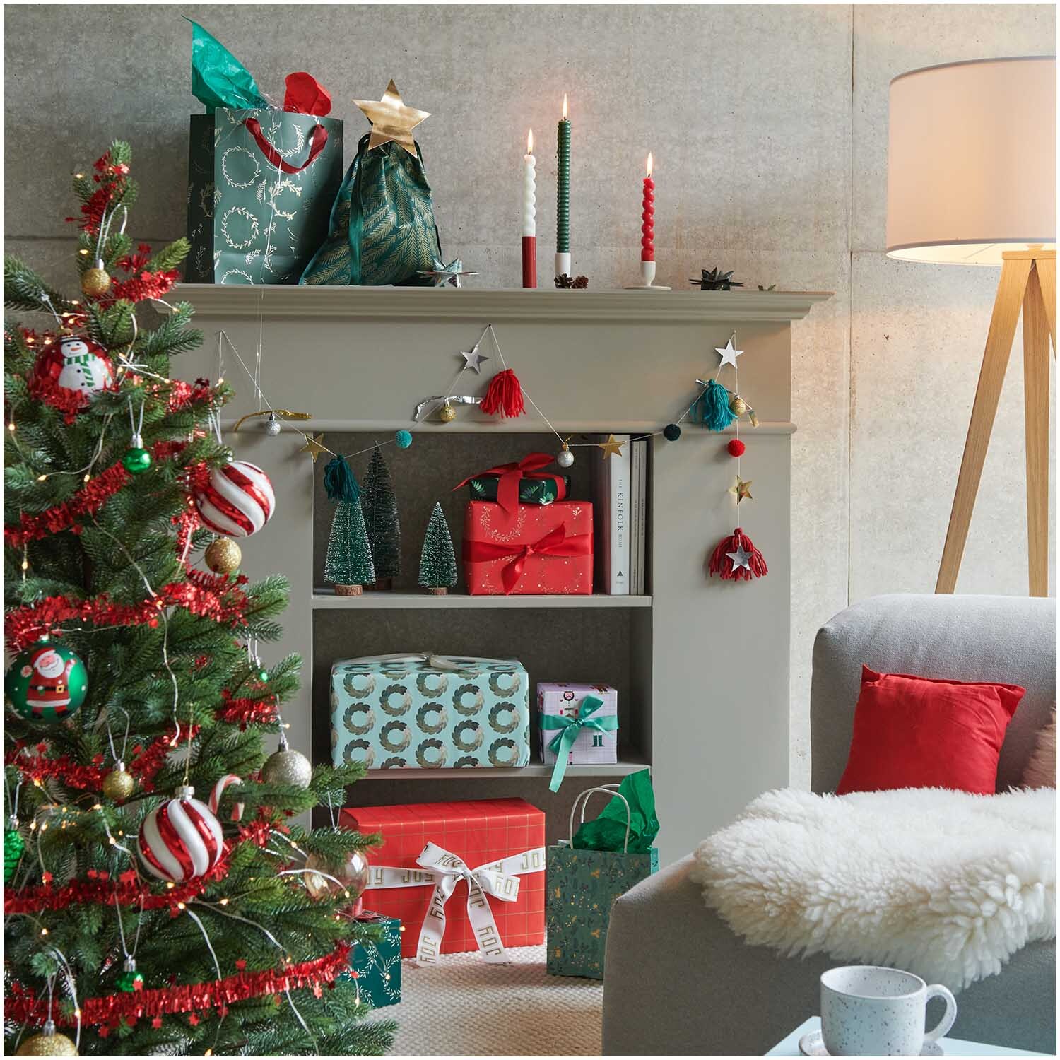 Quasten-Girlande rot-grün 2,2m von Rico Design schmückt ein festlich dekoriertes Wohnzimmer mit Weihnachtsbaum und Geschenken.