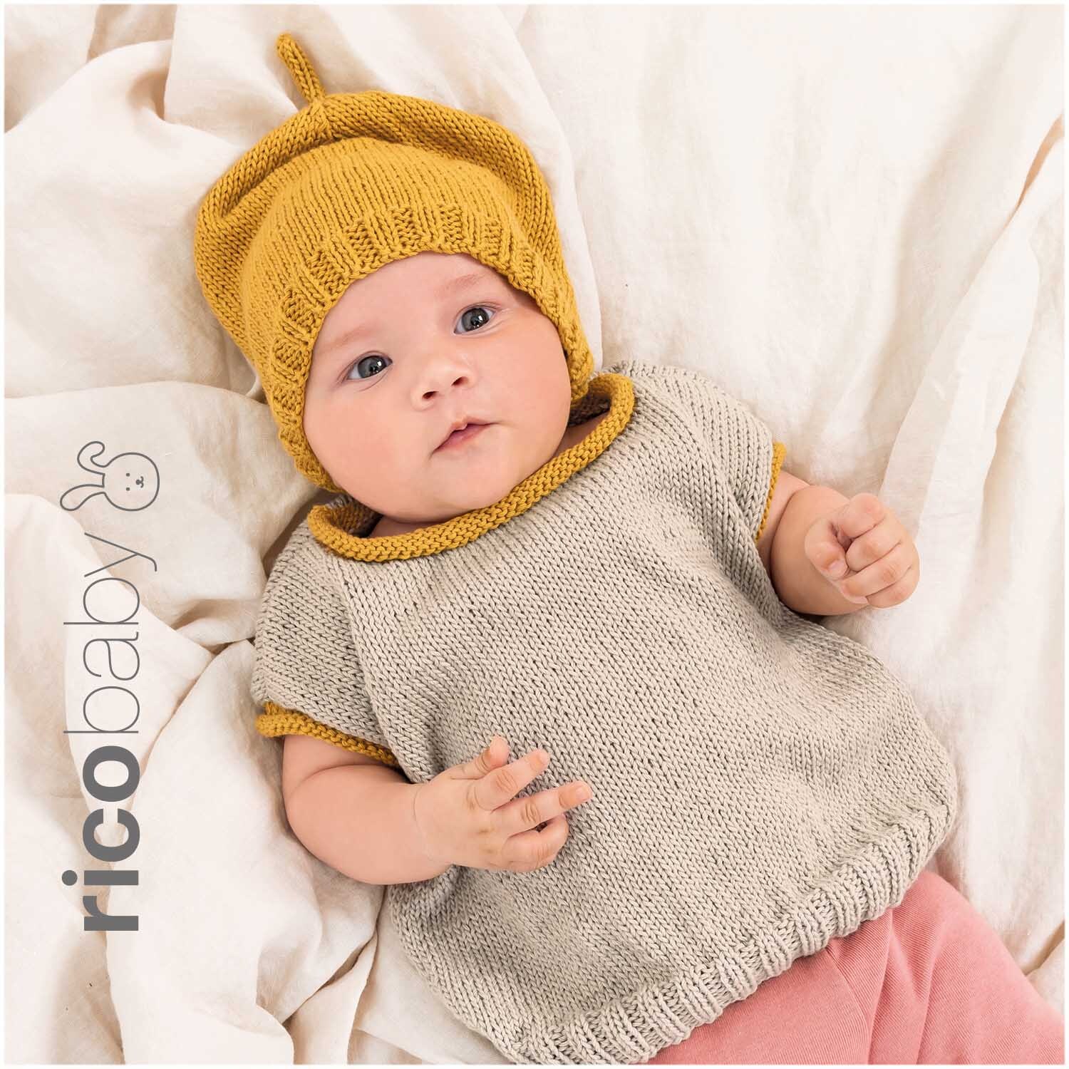 Rico Baby Cotton Soft dk: Baby in gestricktem Outfit mit senffarbener Mütze und beigem Oberteil.