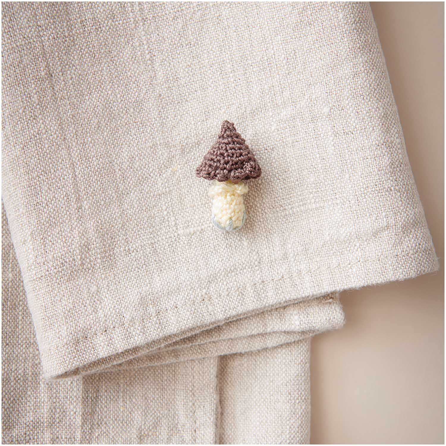 Essentials Crochet: Handgefertigter Pilz-Anstecker auf beigem Stoff, ideal für kreative Projekte.