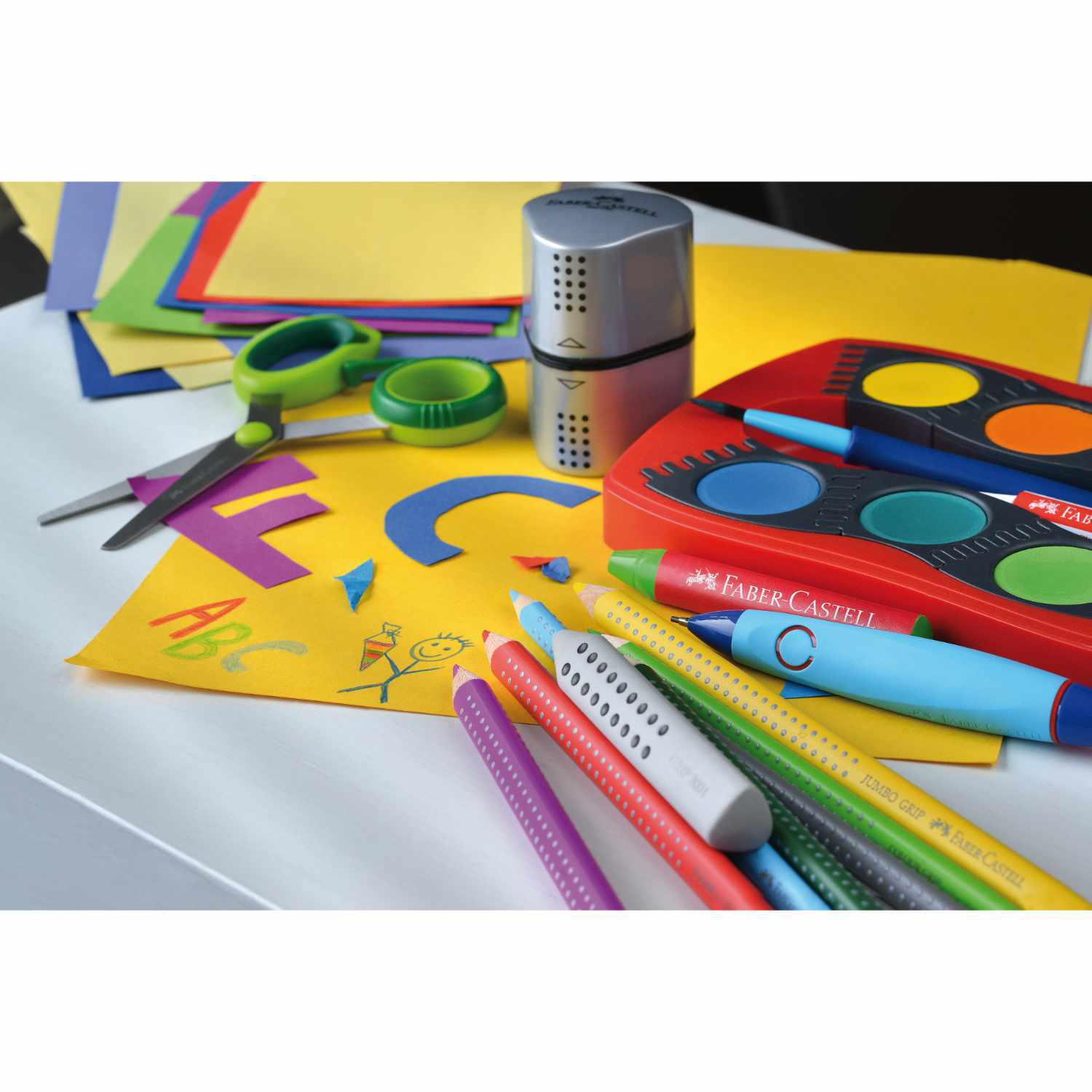 Farbkasten Connector 12 Farben von Faber Castell mit bunten Stiften, Schere und Anspitzer auf einem Tisch.