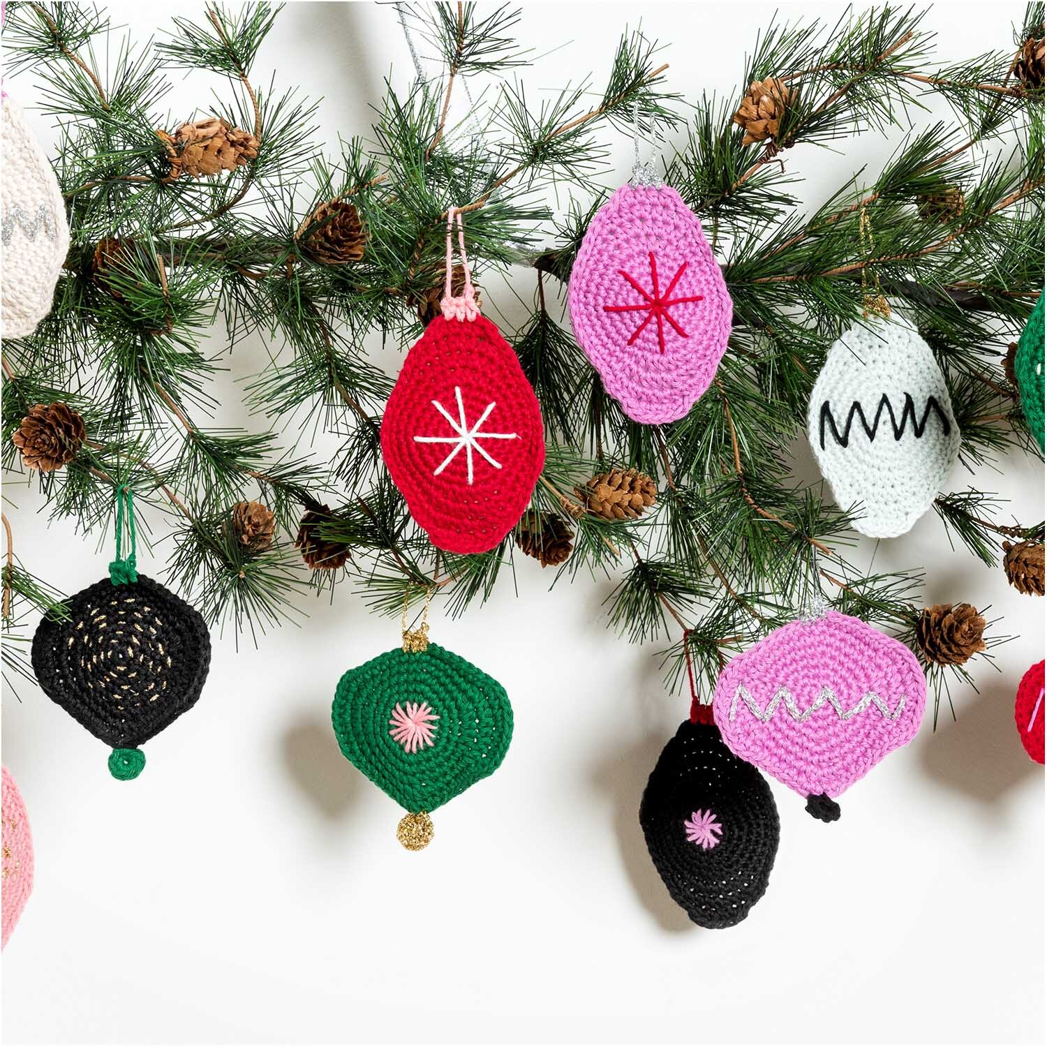 Creative Ricorumi dk: Bunte, gehäkelte Weihnachtsornamente an einem Tannenzweig, ideal für festliche Dekorationen.