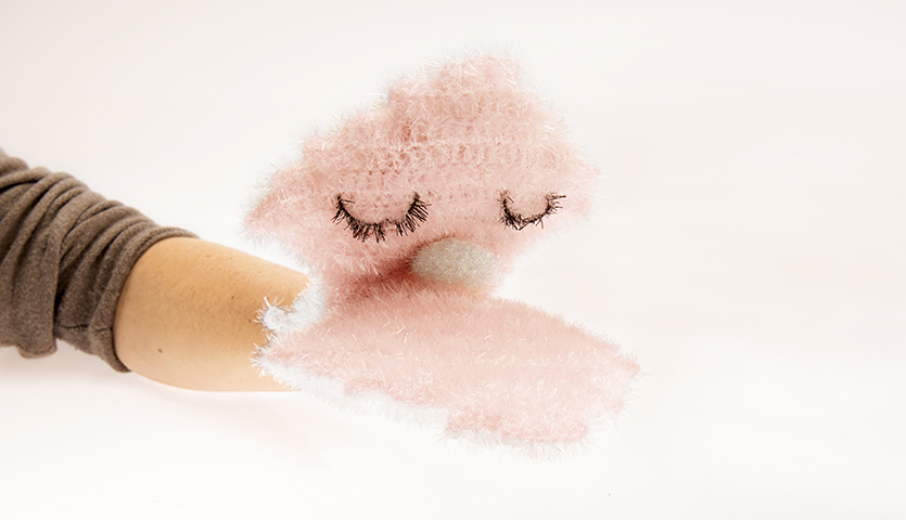 Häkelanleitung Waschhandschuh Muschel: Rosa Waschhandschuh mit geschlossenen Augen auf einem Arm.
