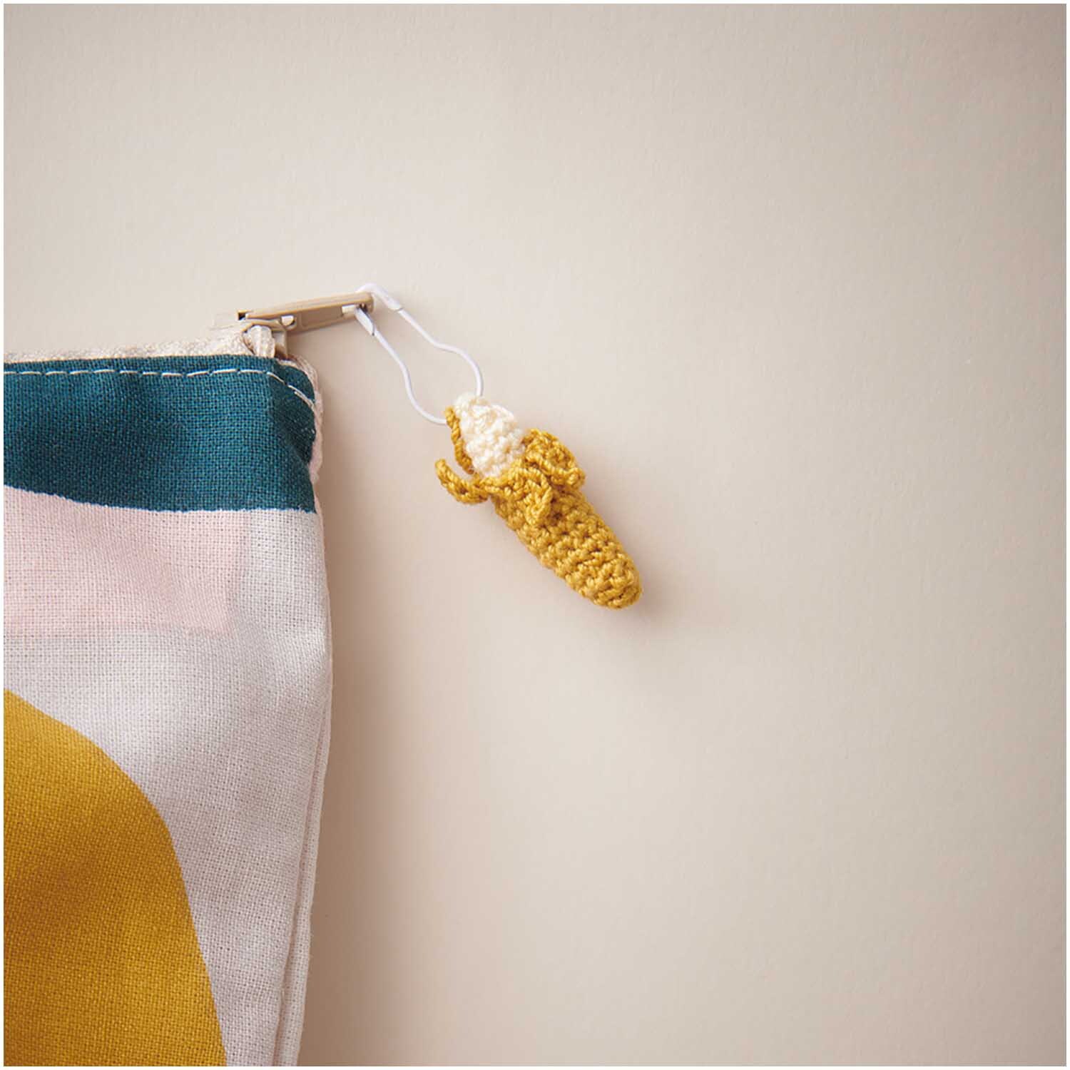 Essentials Crochet: Gehäkelter Bananenanhänger in Vanille von Rico Design, an bunter Tasche befestigt.
