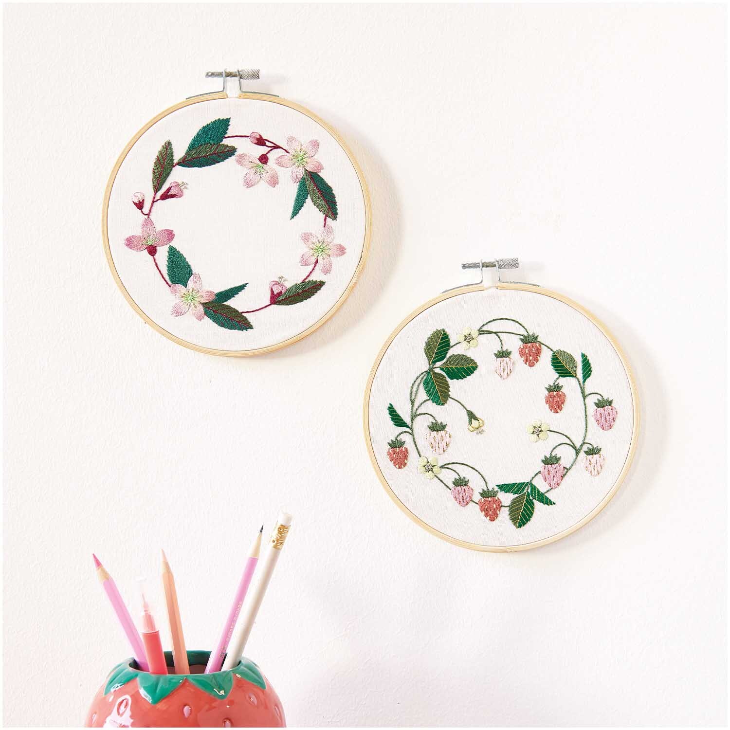 Stickpackung Kirschblütenkranz vorgezeichnet: Zwei Stickrahmen mit floralen Motiven an einer weißen Wand, von Rico Design.