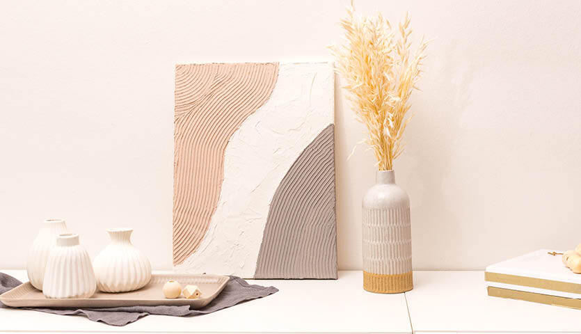 Anleitung Leinwand mit Strukturpaste und Acrylfarben gestalten: Kunstwerk mit Pastelltönen, dekoriert mit Vasen und Trockenblumen auf einem Tisch.