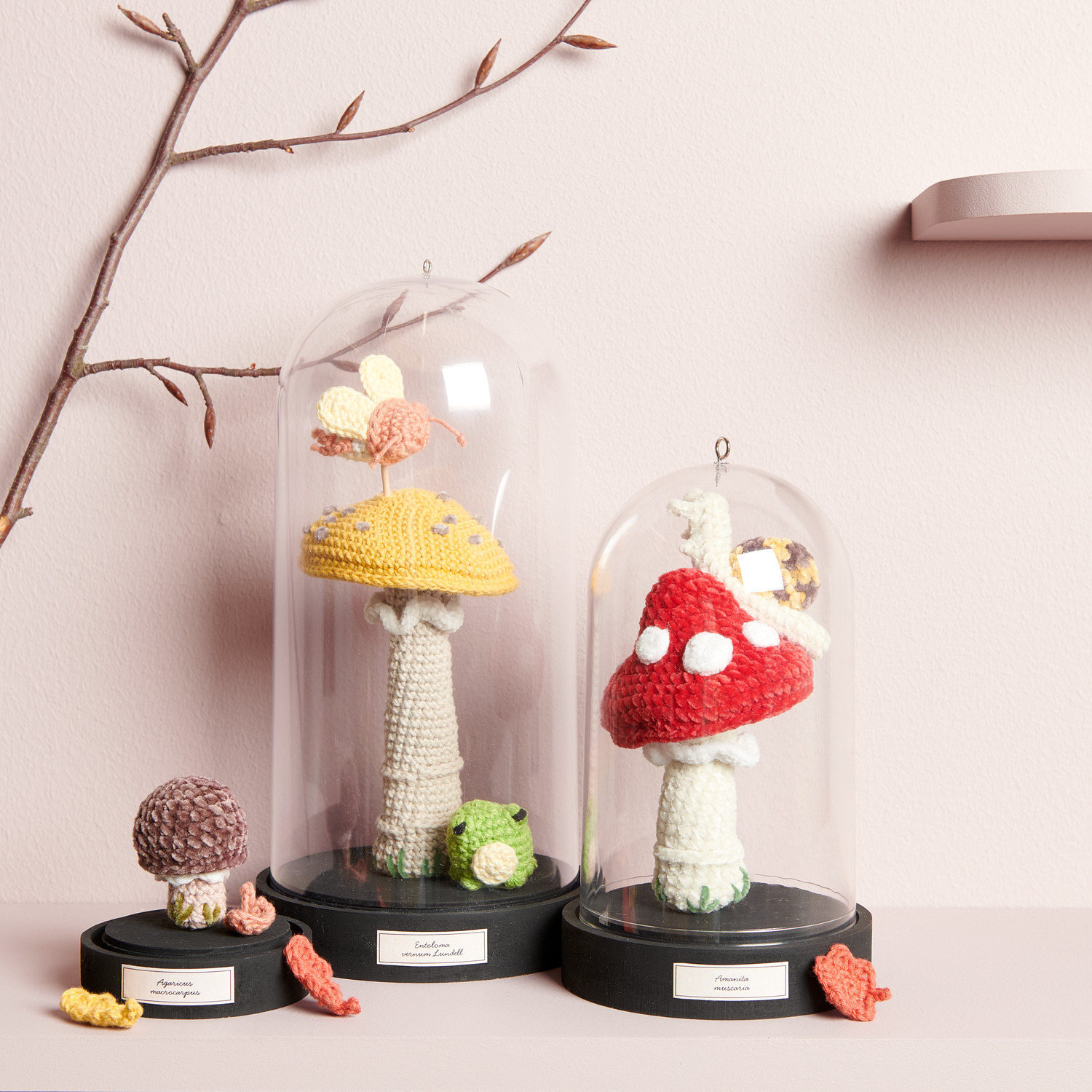 Creative Ricorumi dk: Gehäkelte Pilze in Glasglocken, dekoriert mit bunten Blättern auf schwarzem Sockel.
