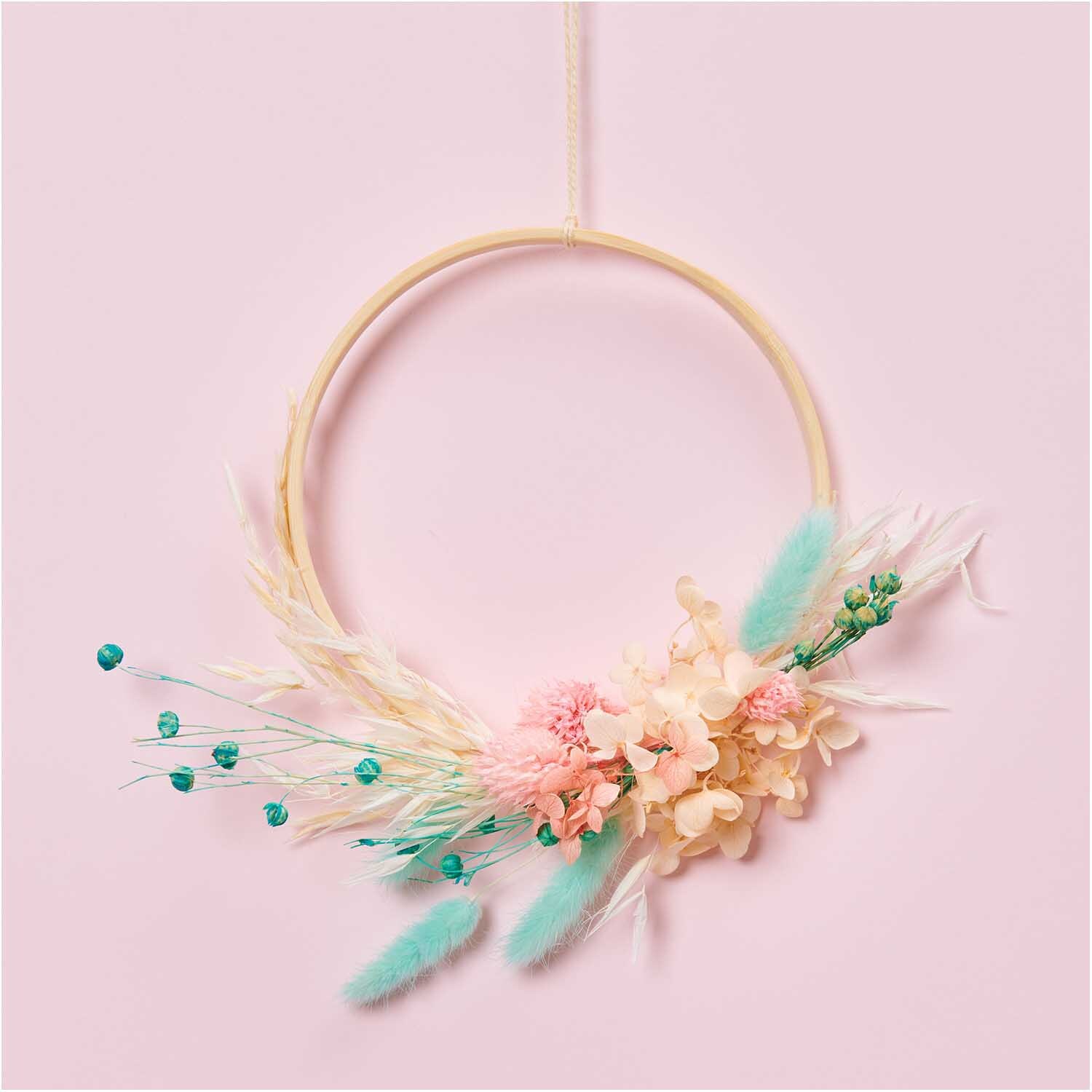 Getrocknete japanische Karde pink 60-75cm 50g von Rico Design, dekorativ in einem Ring mit pastellfarbenen Blumen und Federn arrangiert.