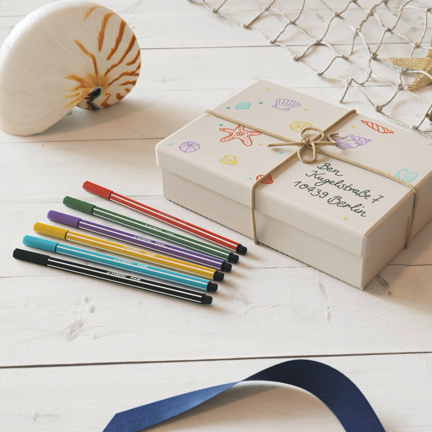 Pen 68, STABILO: Bunte Filzstifte auf hellem Holztisch neben dekorativer Muschel und Geschenkbox.