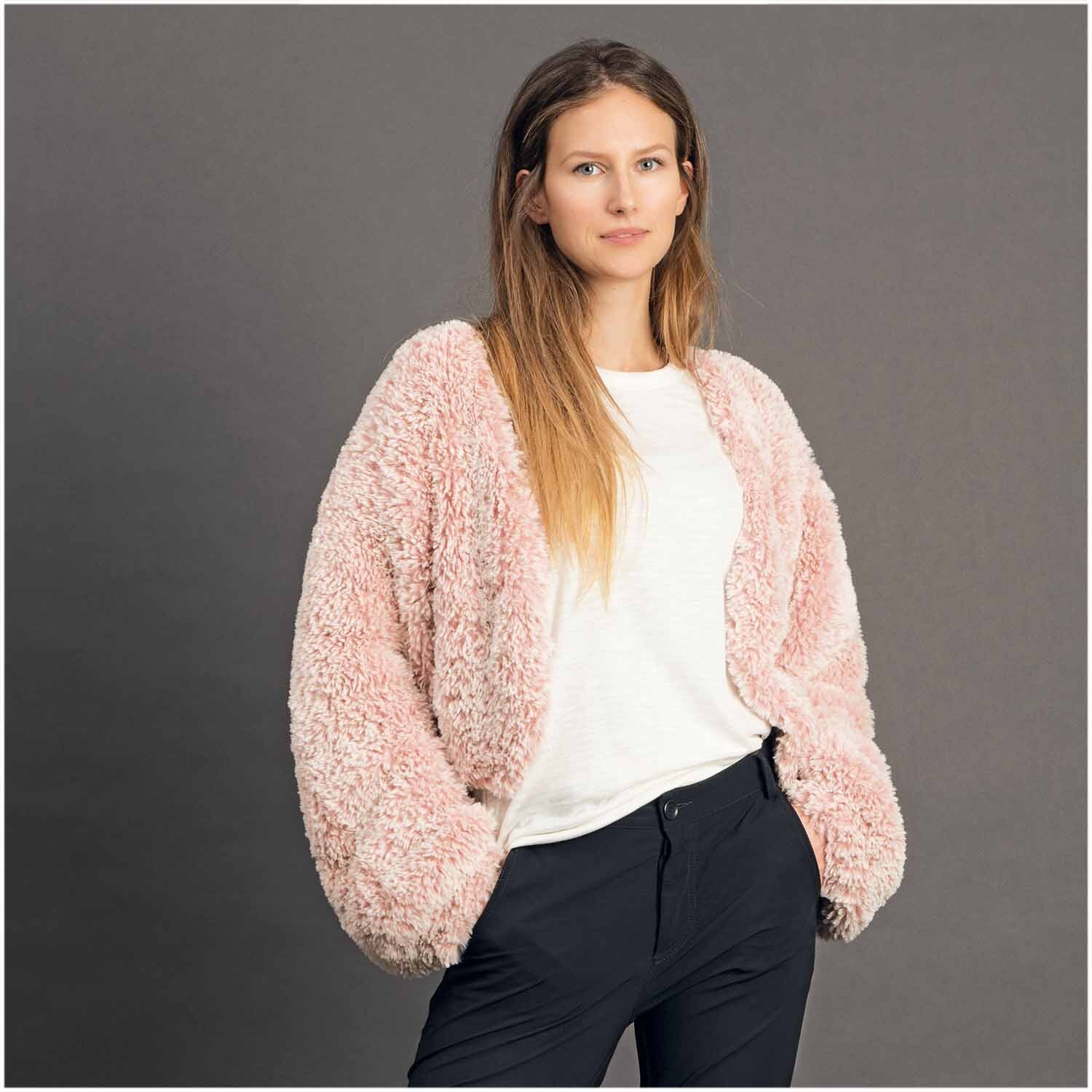 Creative Petit Lapin Super Chunky: Frau trägt flauschige rosa Strickjacke von Rico Design vor grauem Hintergrund.
