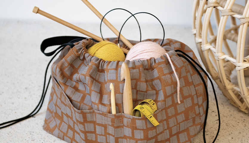 Nähanleitung Handarbeitstasche: Eine gemusterte Tasche mit Stricknadeln, Garn und Maßband. Ideal für Handarbeitsprojekte.