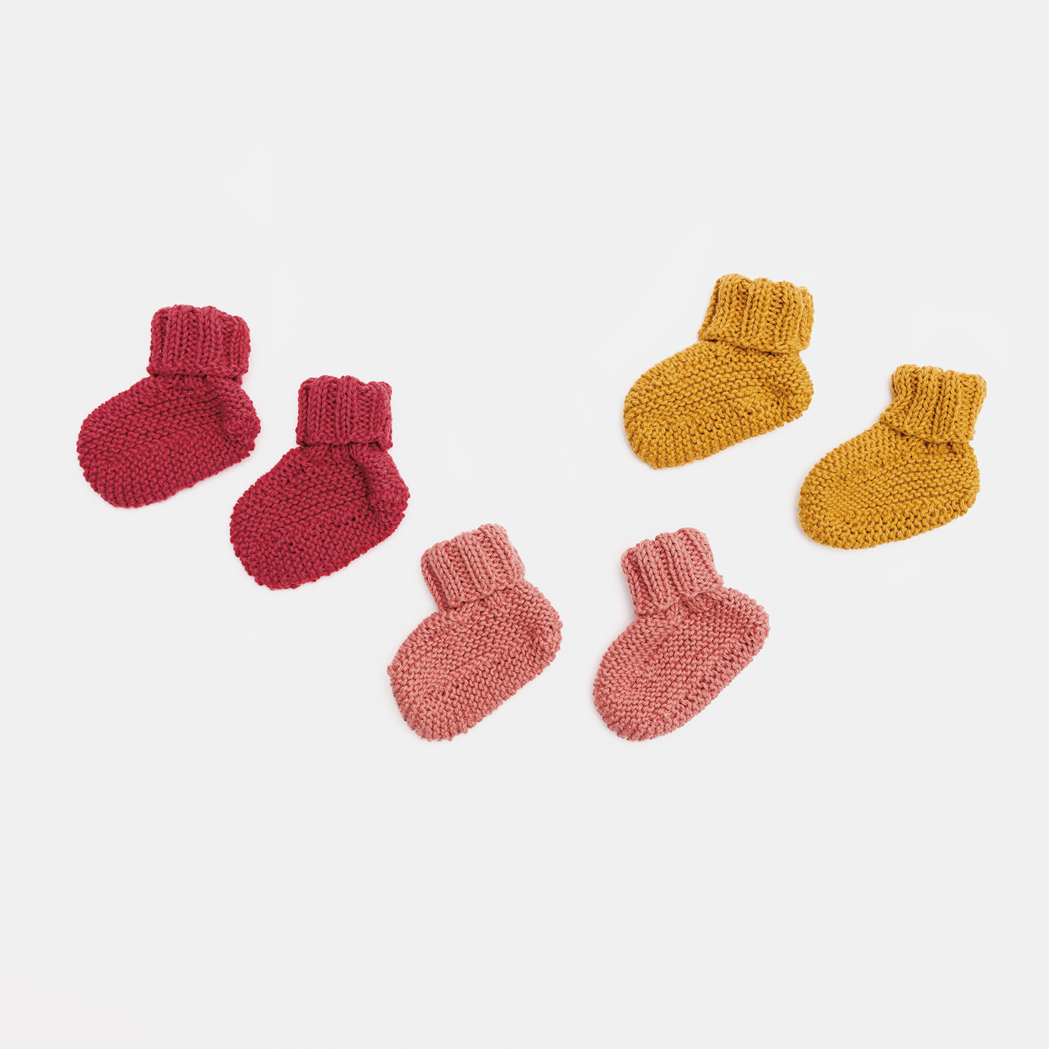 Strickanleitung Babysocken aus Baby Cotton Soft dk: Drei Paar gestrickte Babysocken in Rot, Gelb und Rosa auf weißem Hintergrund.