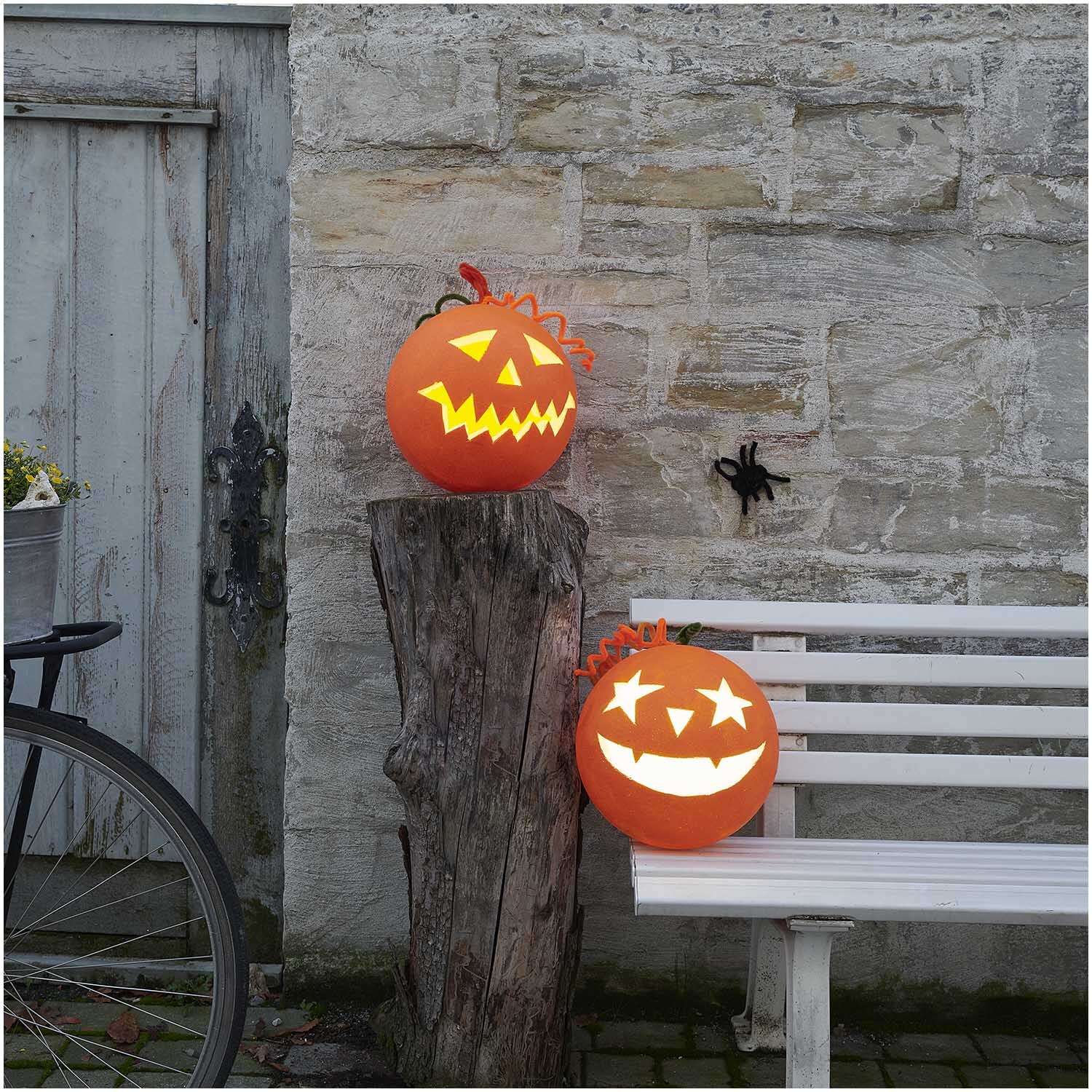 Polystyrol Kugel 30cm von Rico Design, dekoriert als leuchtender Halloween-Kürbis auf Holzstumpf und Bank.