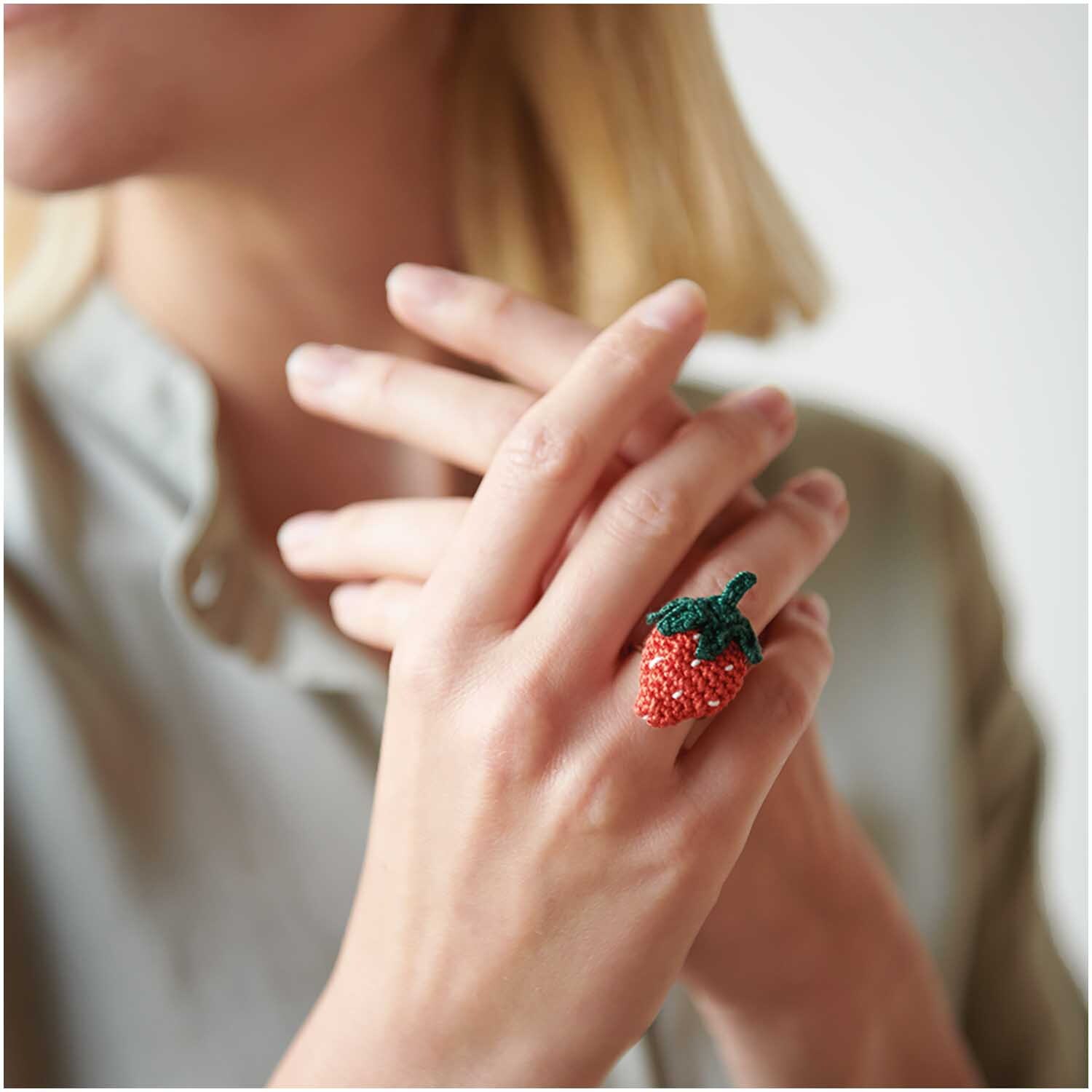 Essentials Crochet: Frau trägt einen handgemachten Erdbeer-Ring. Perfekt für kreative Projekte.