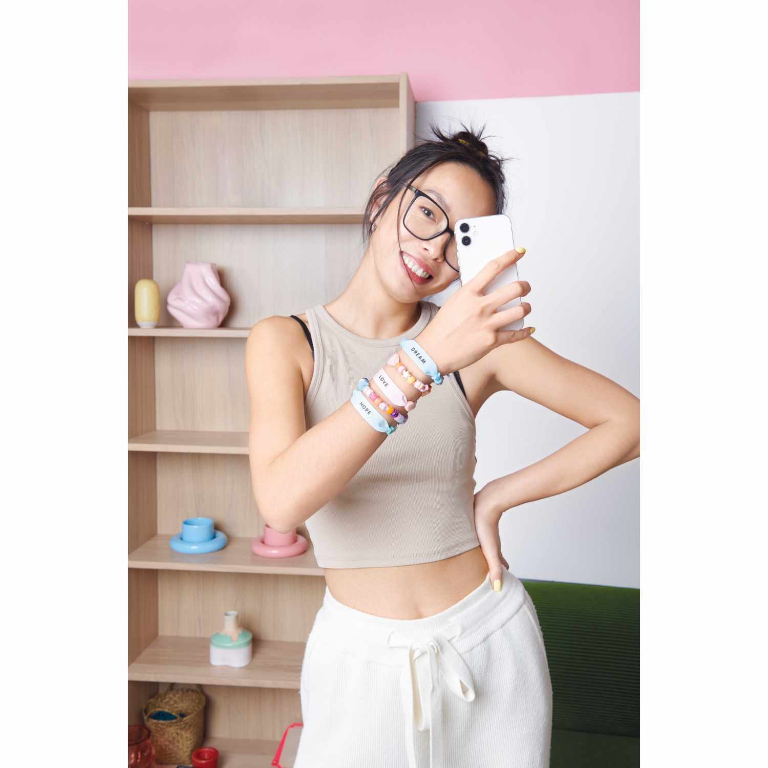 itoshii - Ponii Beads Bügelmotiv Schriftzüge 8 Designs. Junge Frau mit Armbändern macht ein Selfie vor einem Regal mit Deko.