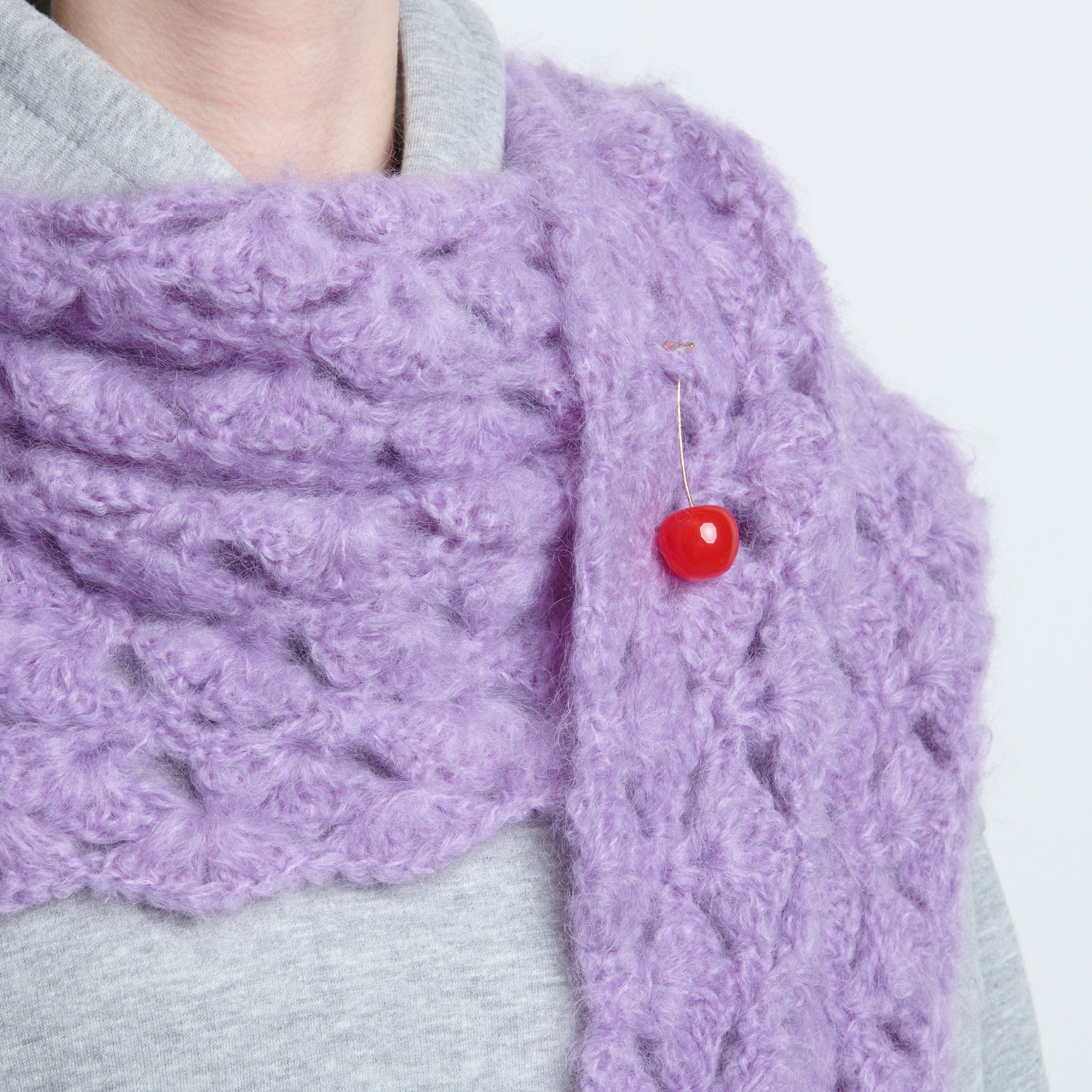 Pin Kirsche: Ein roter Kirschen-Pin von Rico Design auf einem flauschigen, lila Schal befestigt.