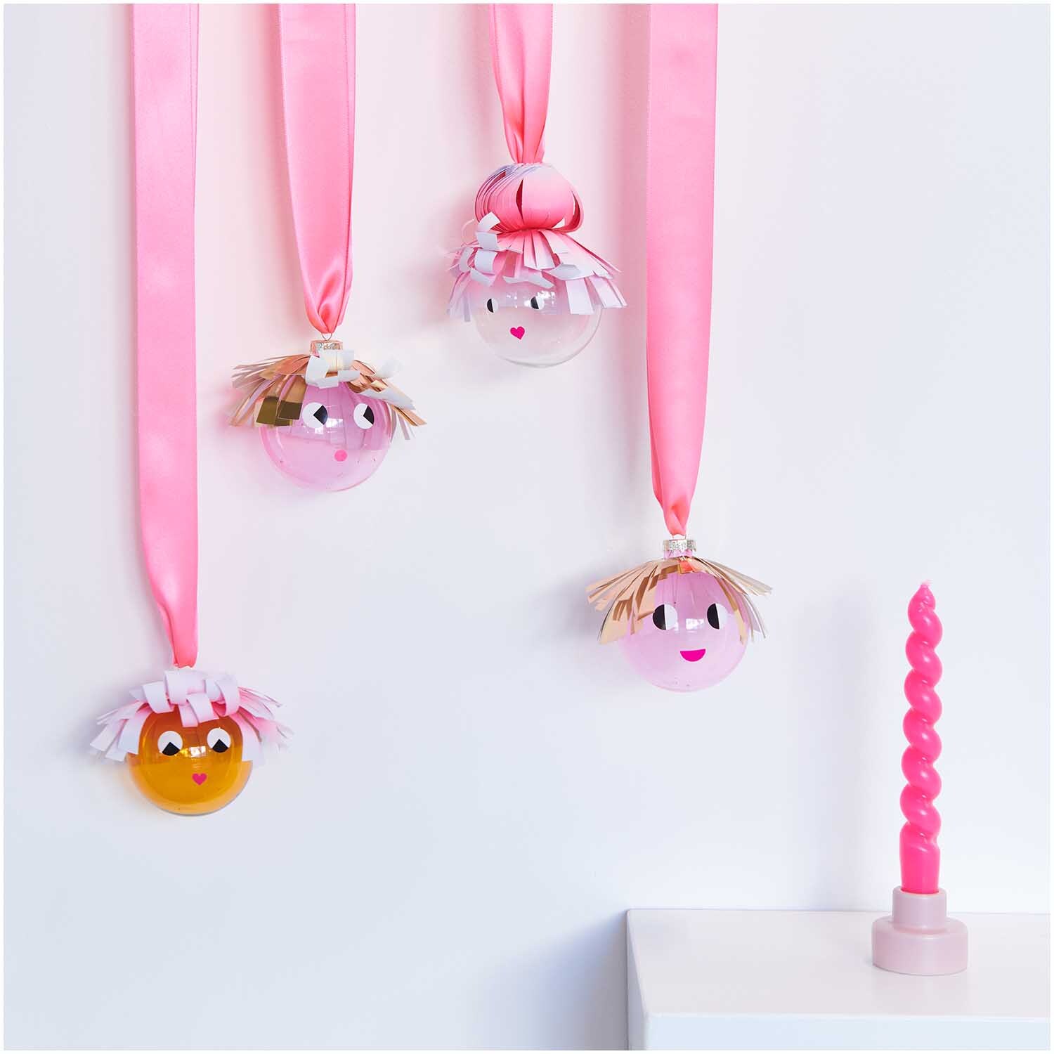 Glaskugel Baumschmuck einfarbig 8cm: Vier dekorative Kugeln mit Gesichtern, aufgehängt an rosa Bändern, neben einer rosa Kerze.
