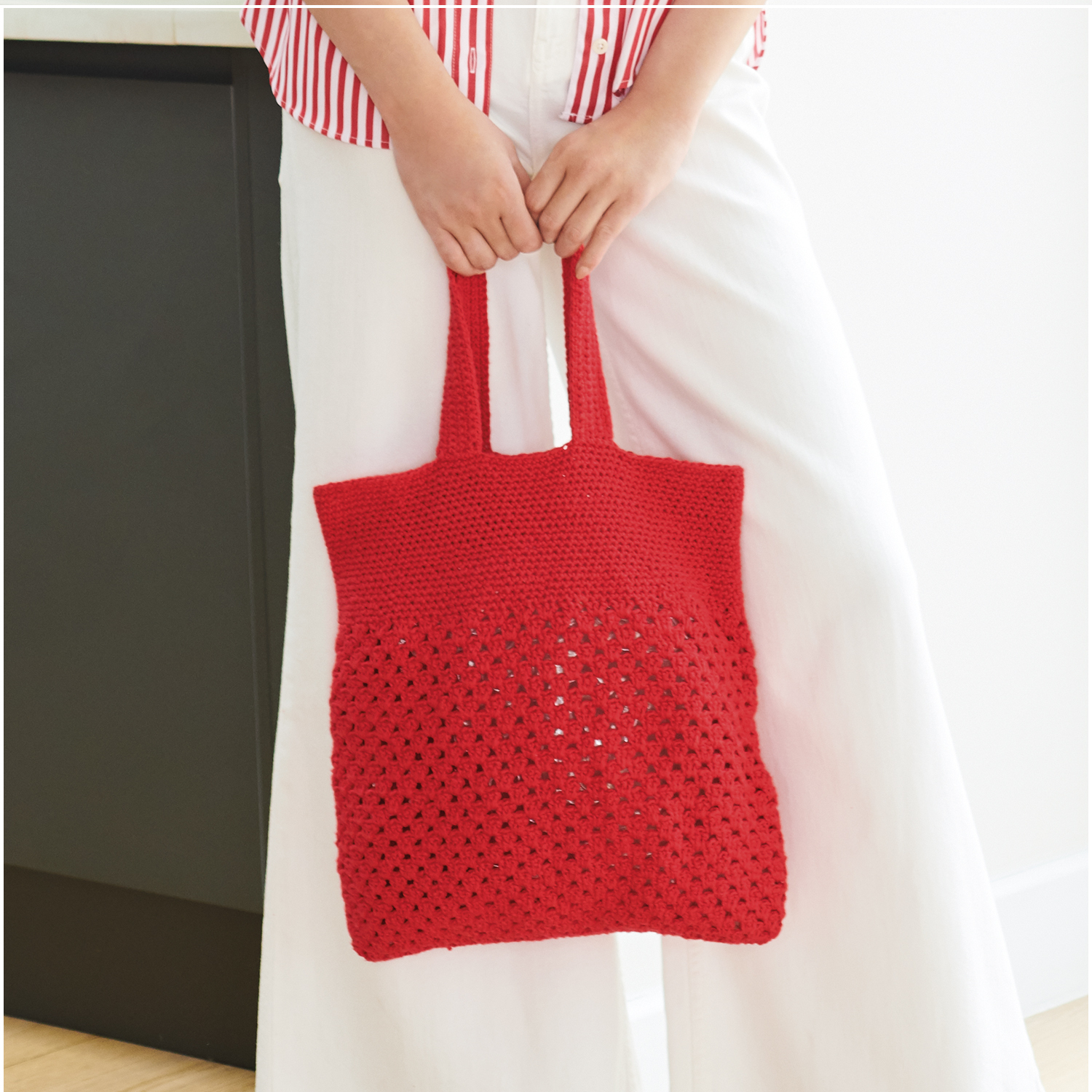 Häkelset Tasche Modell 03 aus Lovewool Nr. 18: Rote, gehäkelte Tasche mit Lochmuster, gehalten von Person in weißer Hose.
