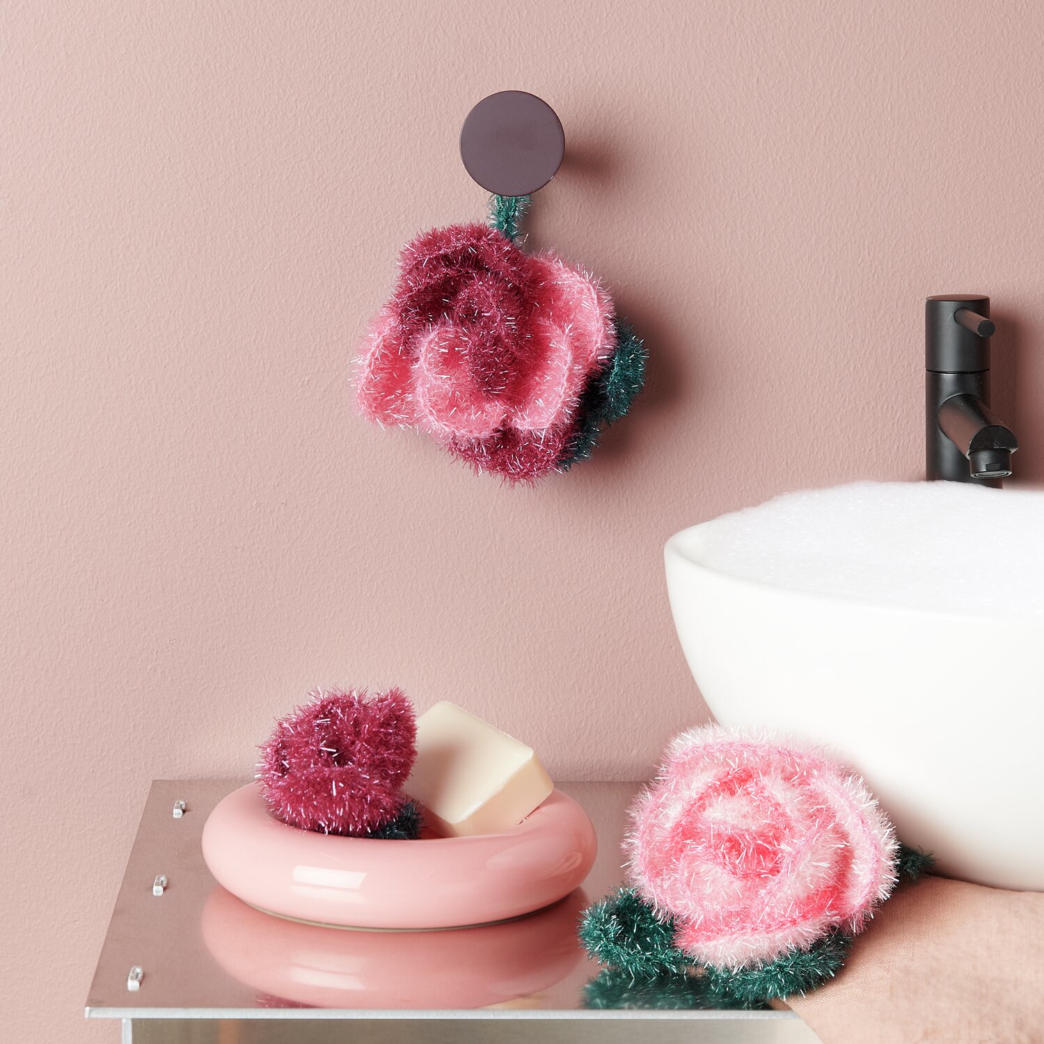 Häkelset Creative Bubble Rose Classic: Flauschige rosa und rote Schwämme in Rosenform, dekorativ im Bad platziert.
