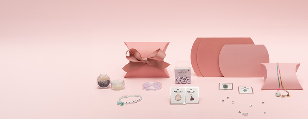 Mehrere pinke Geschenkschachteln mit Schmuckperlen, Schmuckband und verschiedenen Anhängern. Fotosetting rosa Wand.