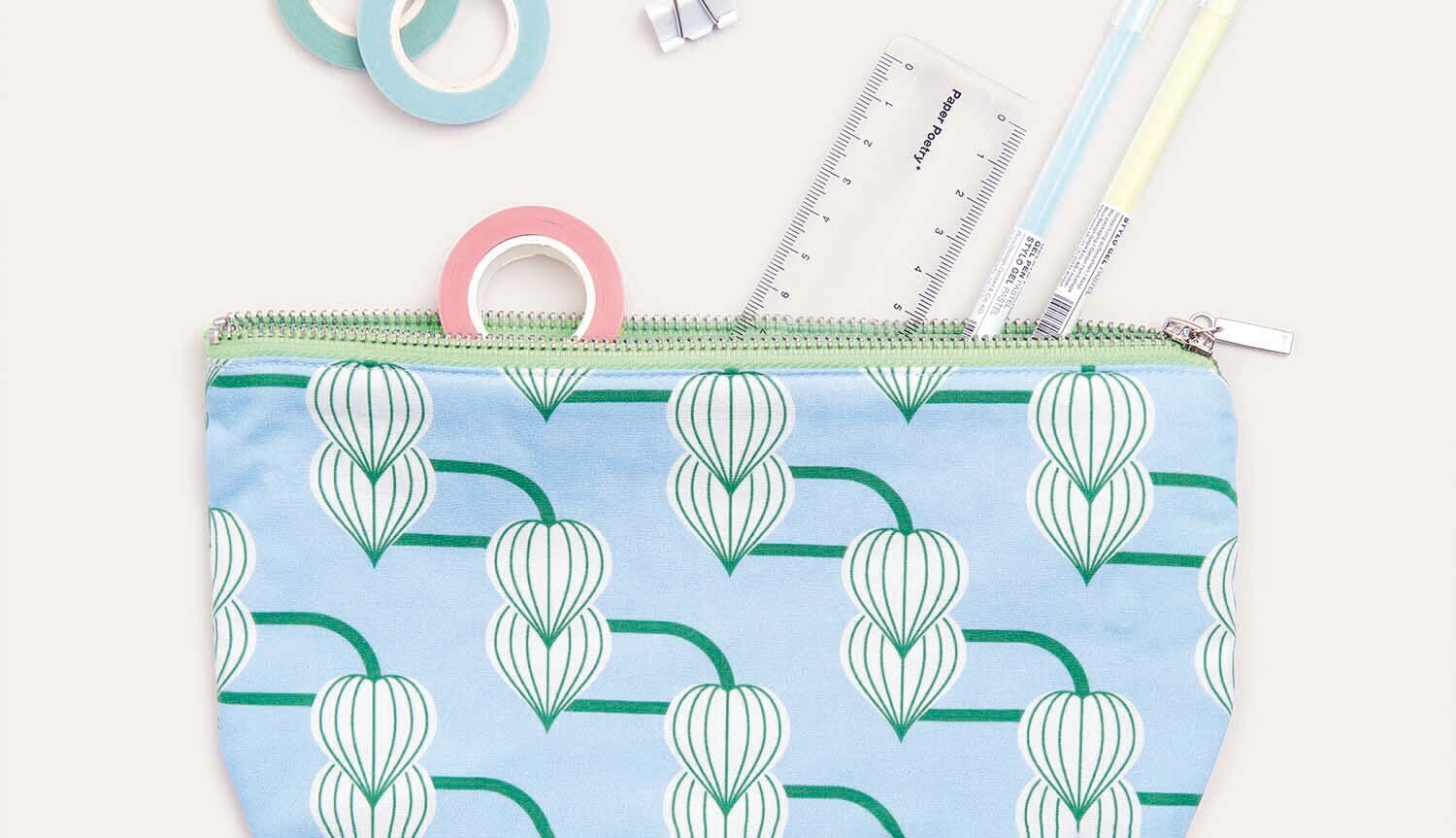 Nähanleitung Etui in Halbmondform: Hellblaues Etui mit grünem Muster, umgeben von Nähzubehör.