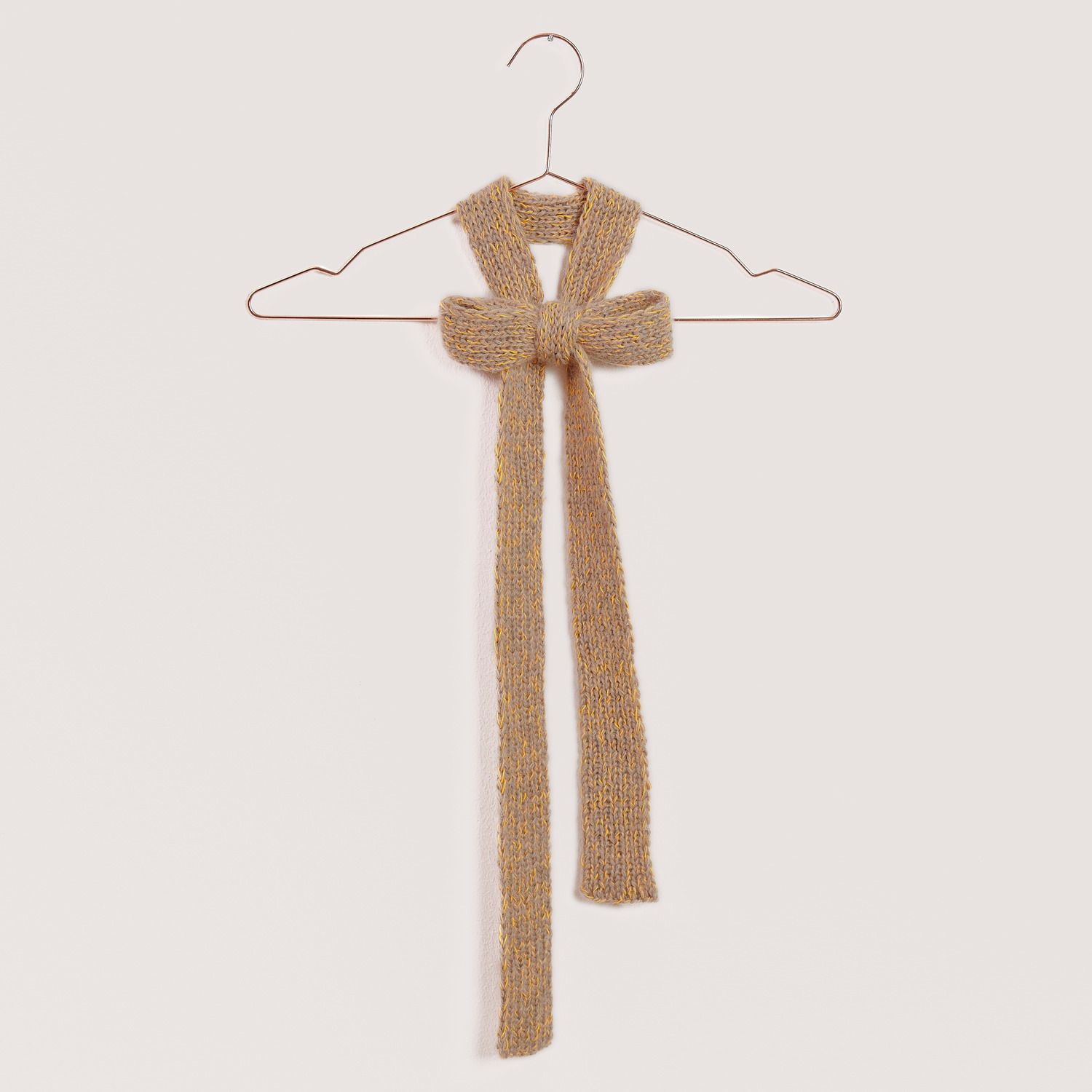Strickset Schleife Modell 11 aus Mini Tücher Special in Beige, präsentiert auf einem Kleiderbügel.