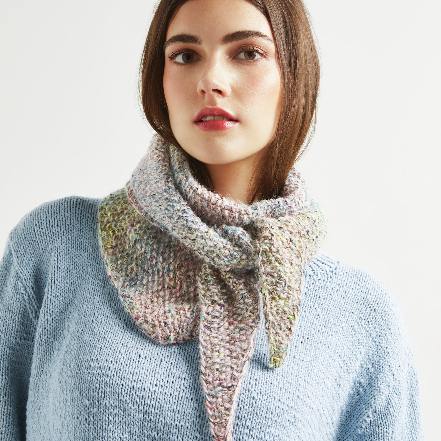 Strickset Dreieckstuch Modell 01a: Frau trägt ein gestricktes Tuch in sanften Farben, passend zu einem hellblauen Pullover.