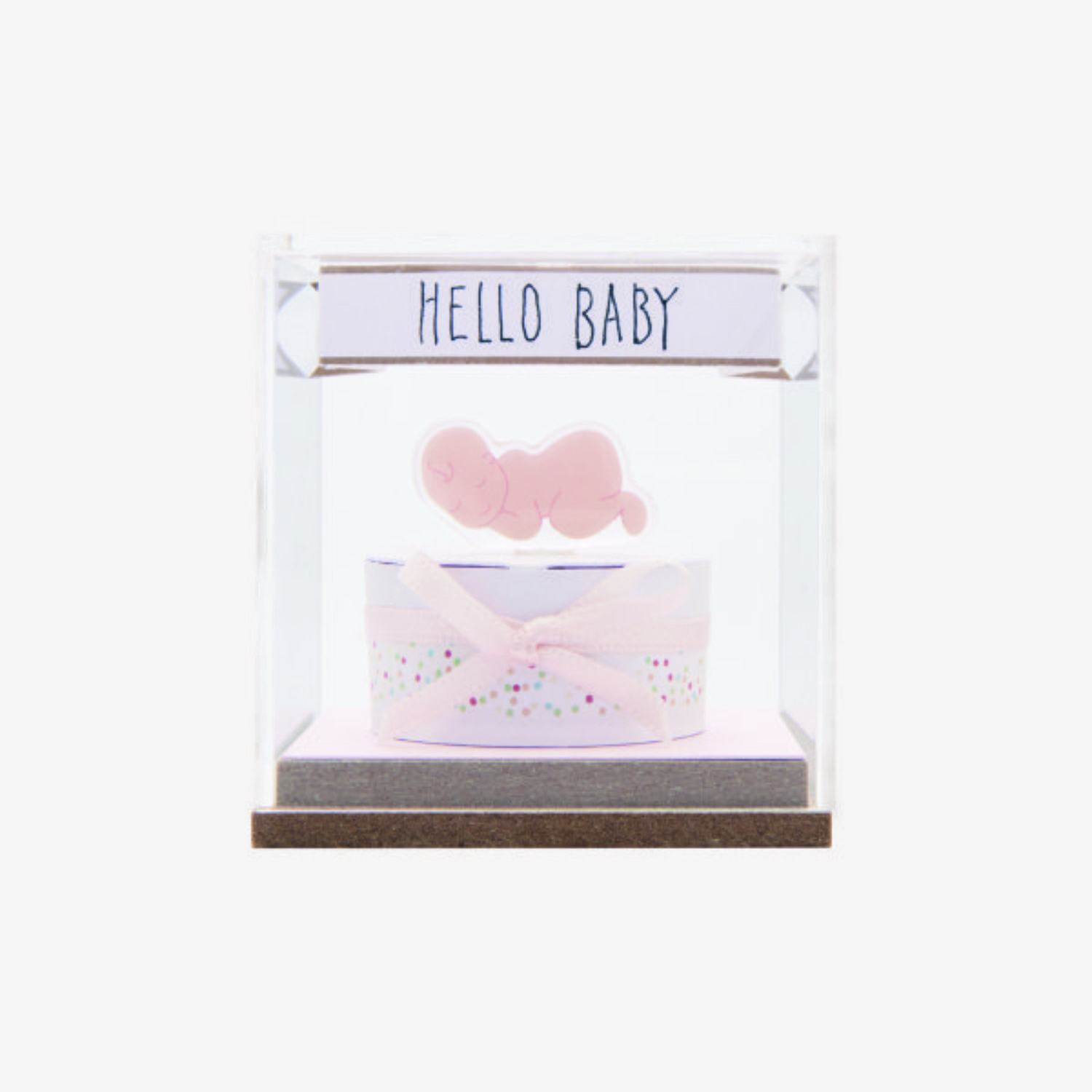 Kleine Dekohaubemit gebastelter Torte und Baby-Gelsticker, sowie ein Etikett mit schwarzem Schriftzug „HELLO BABY“. Fotosetting weiße Wand.