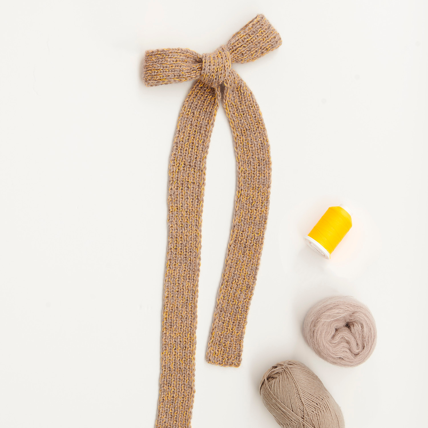 Mini Tücher Special: Beigefarbene Strickschleife mit Garnrollen und Nähgarn auf hellem Hintergrund.