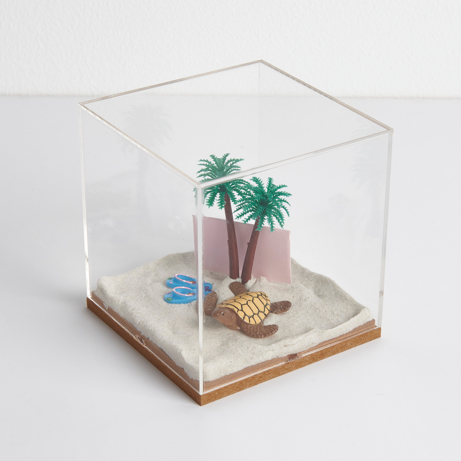Figurico Dekohaube Würfel zeigt Miniatur Schildkröte, Flip Flops und Palmen auf Sand.