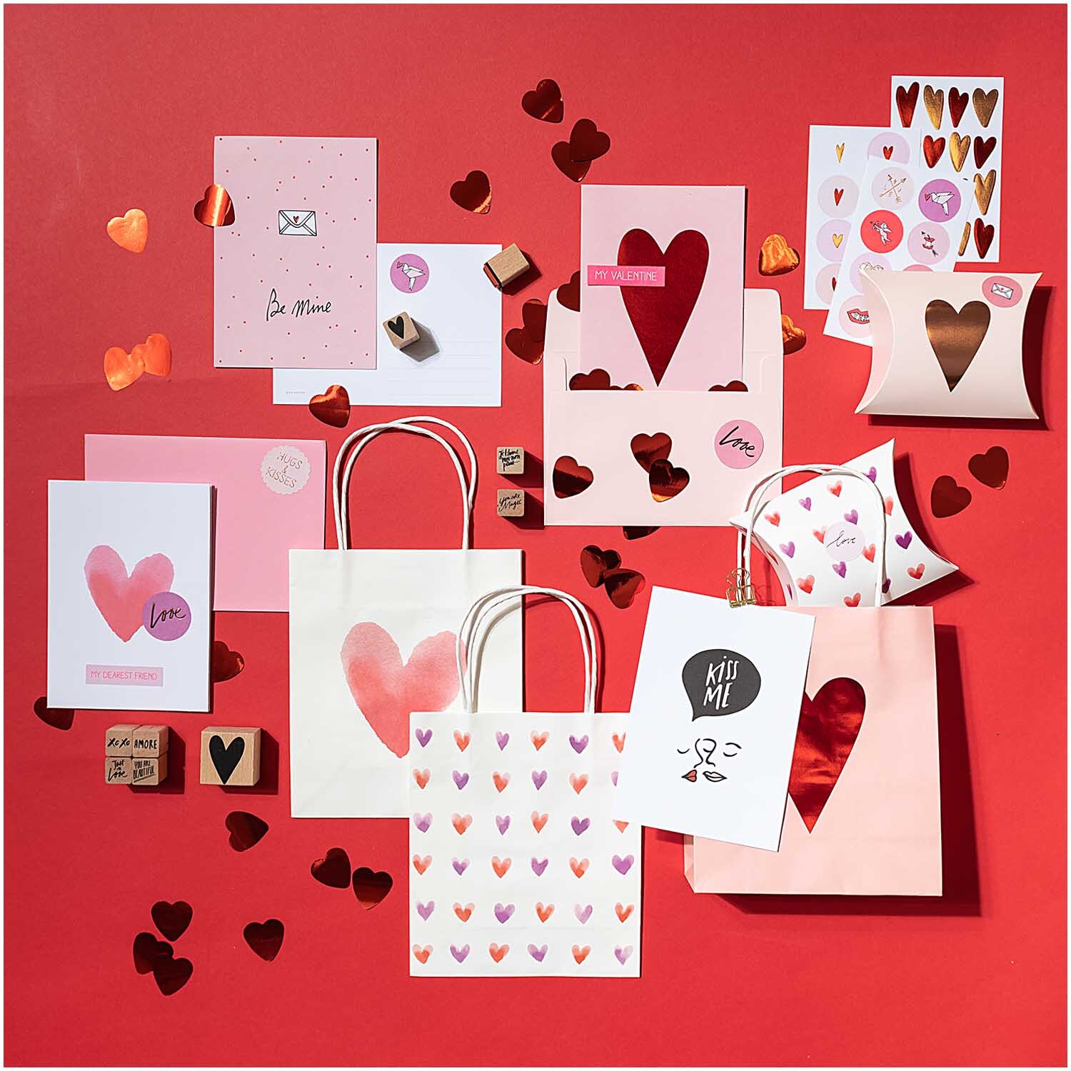 Paper Poetry Sticker It must be love: Verschiedene rote und rosa Herzsticker und Geschenktüten auf rotem Hintergrund.