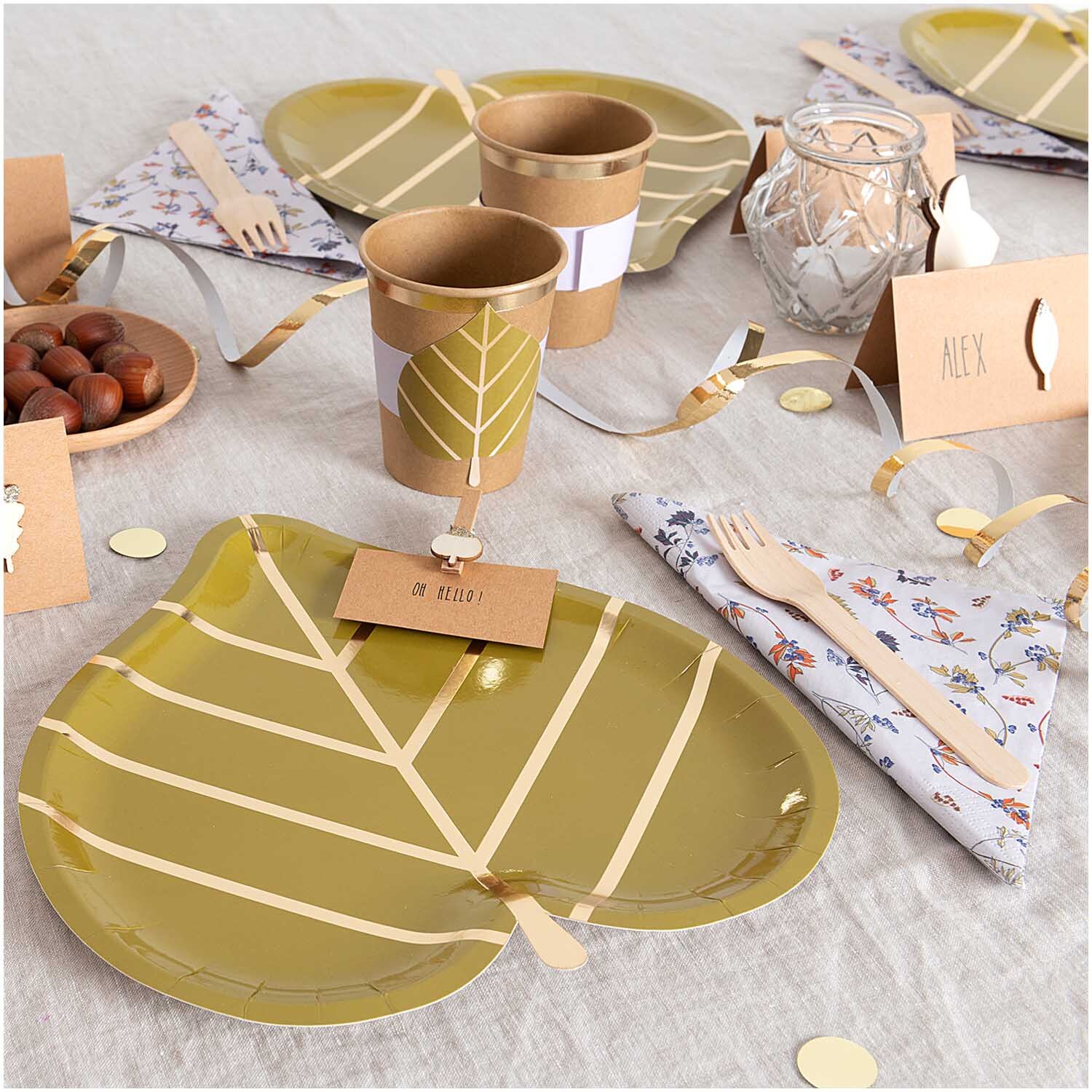 Pappteller Blatt 24,3x26,5cm 12 Stück von Rico Design auf einem gedeckten Tisch mit grünem Blattmuster, umgeben von Partyzubehör.