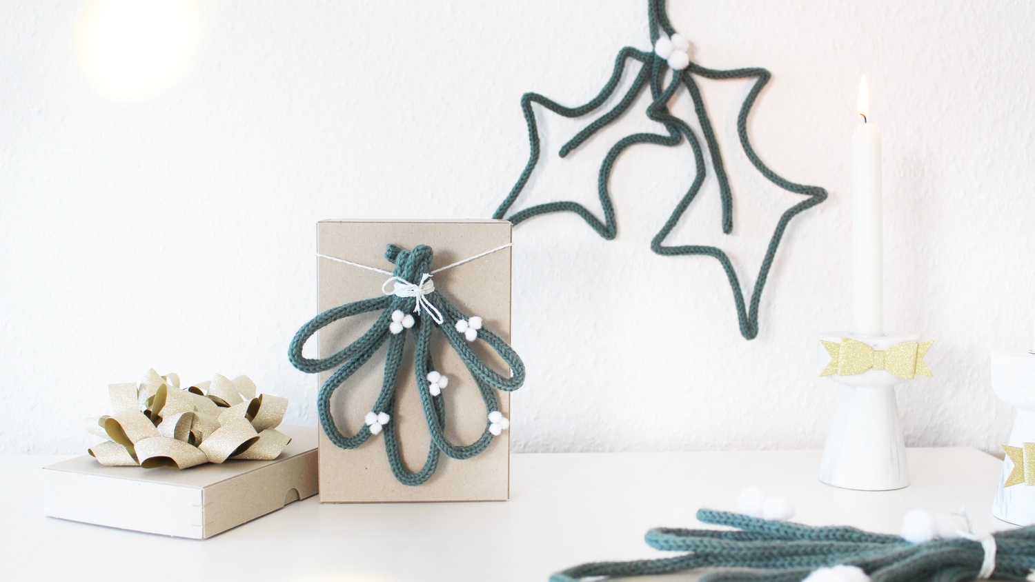Inspiration DIY Mistelzweig mit der Strickmühle @tinkerhome: Dekoratives Set aus grünen Strickzweigen und weißen Akzenten auf einem Geschenk.