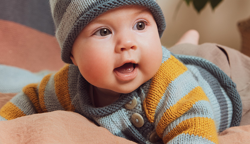 Strickanleitung Babypullover und Mütze: Baby trägt gestreiften Pullover und Mütze aus weichem Garn.