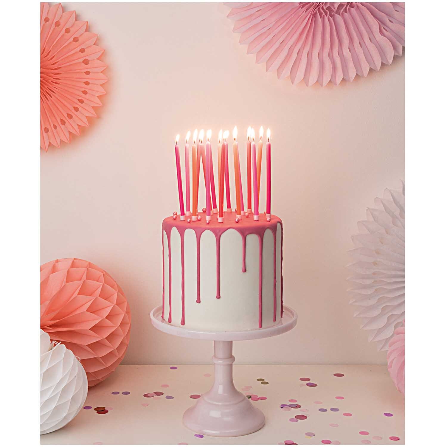 Wabenpapier Bälle Sommer 3 Stück: Ein weißer Kuchen mit rosa Kerzen, umgeben von rosa Wabenpapier-Dekorationen. Perfekt für festliche Anlässe.