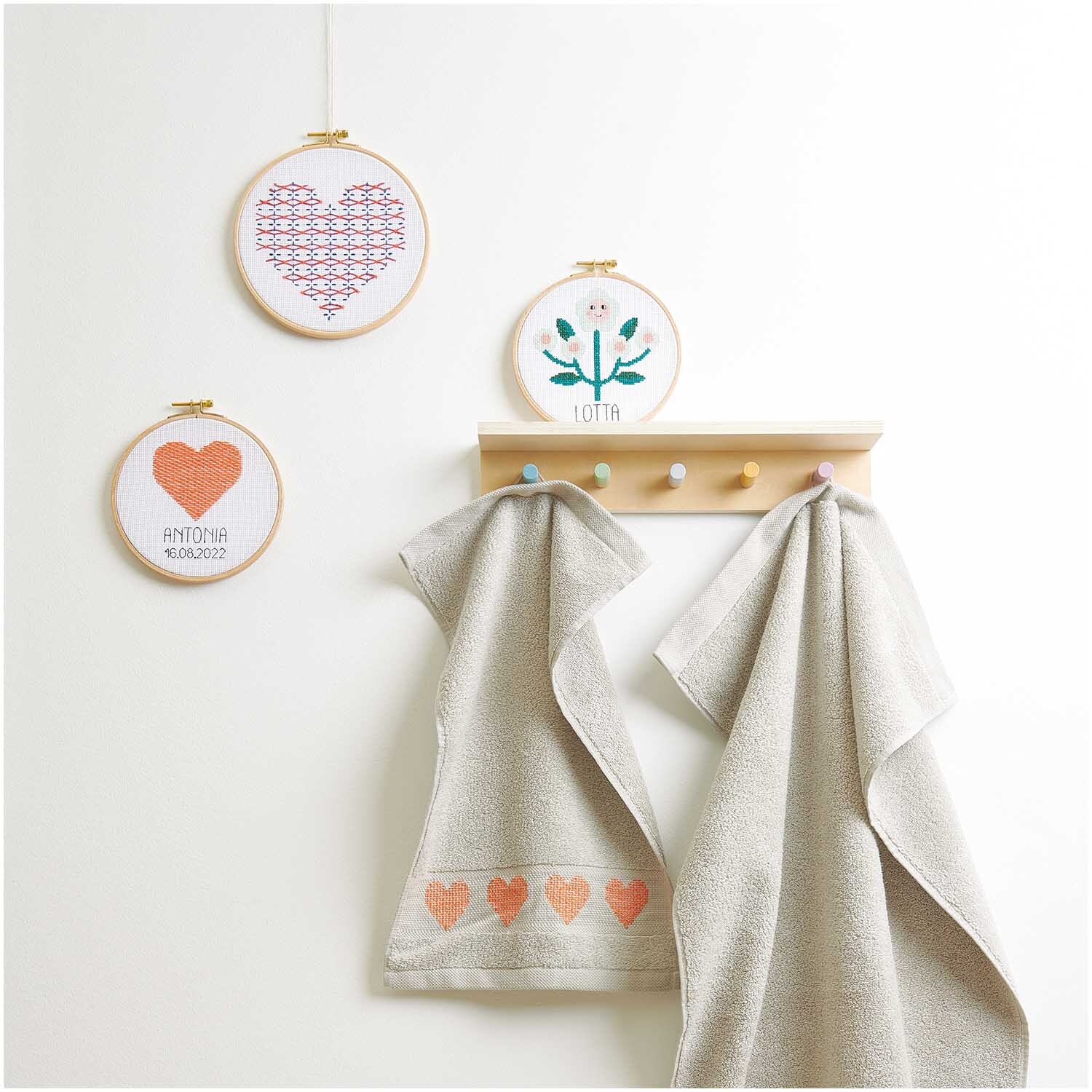 Stickpackung Sashiko Herz: Drei bestickte Rahmen mit Herz- und Blumenmotiven, zwei Handtücher darunter.