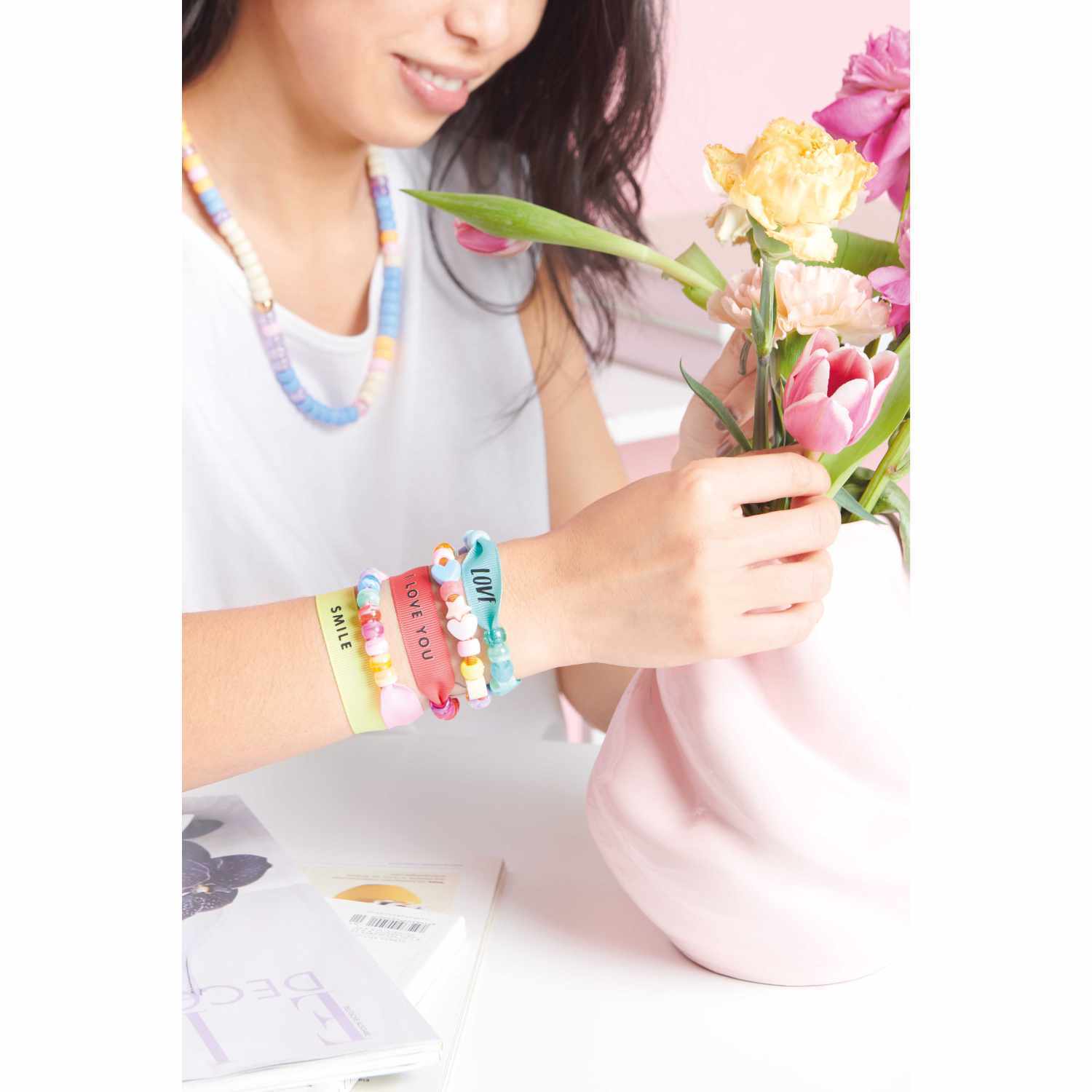 Itoshii - Ponii Beads Bügelmotiv Slogans: Frau arrangiert Blumen in Vase, trägt bunte Armbänder.