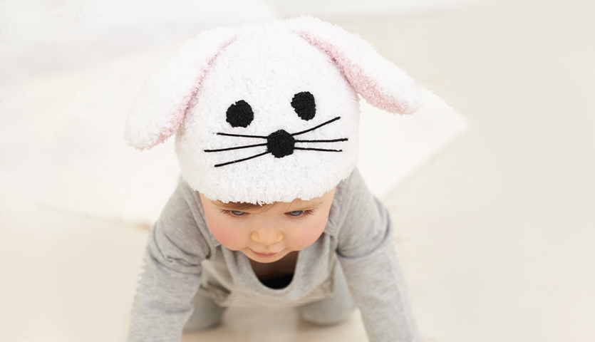 Strickanleitung Babymütze mit Hasenohren: Baby trägt weiße Mütze mit Hasenohren und schwarzen Details.