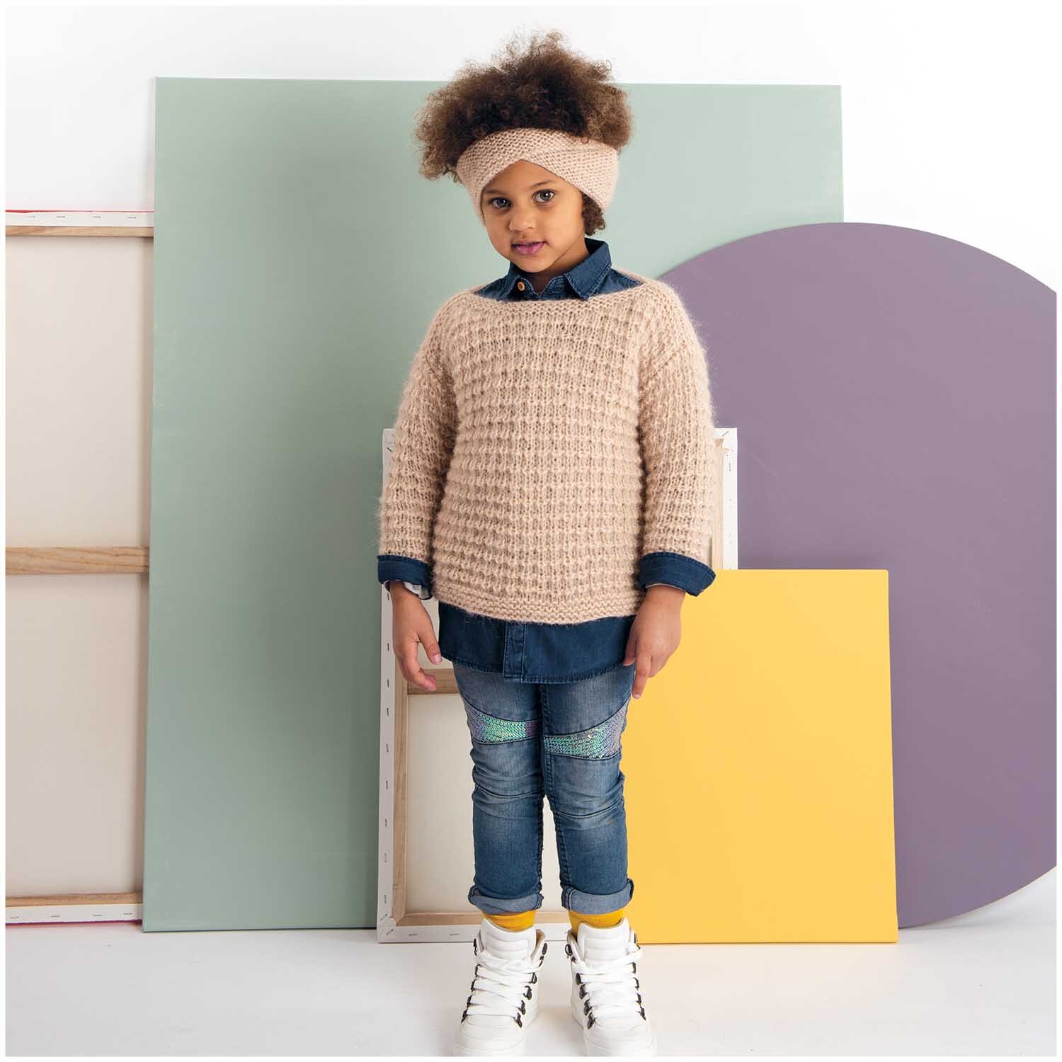 Fashion Daiyamondo: Kind in gestricktem Pullover und Stirnband, vor buntem Hintergrund stehend.